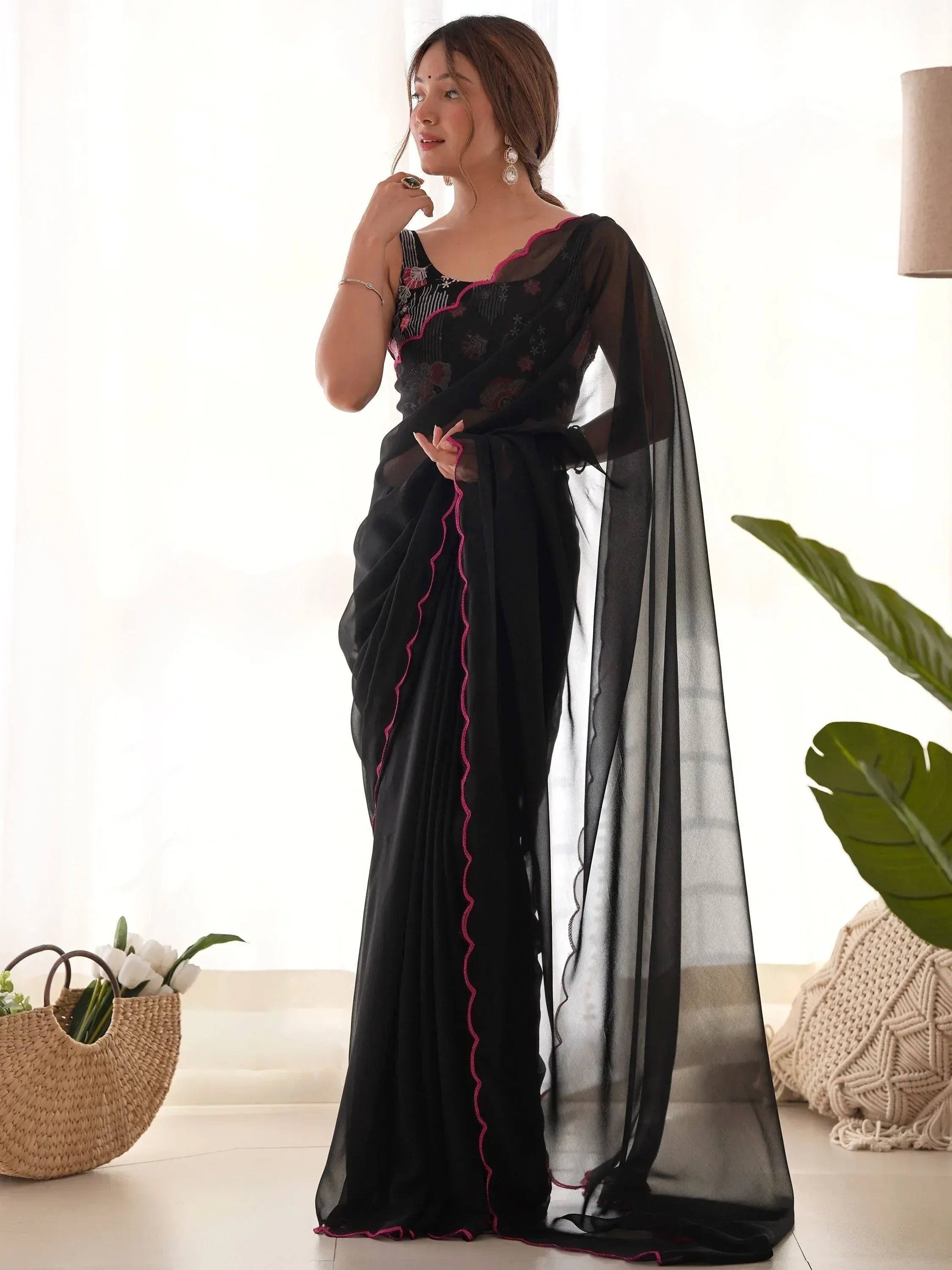 Black sheer saree with pink embroidery and scalloped border, styled with floral blouse for ethnic wear