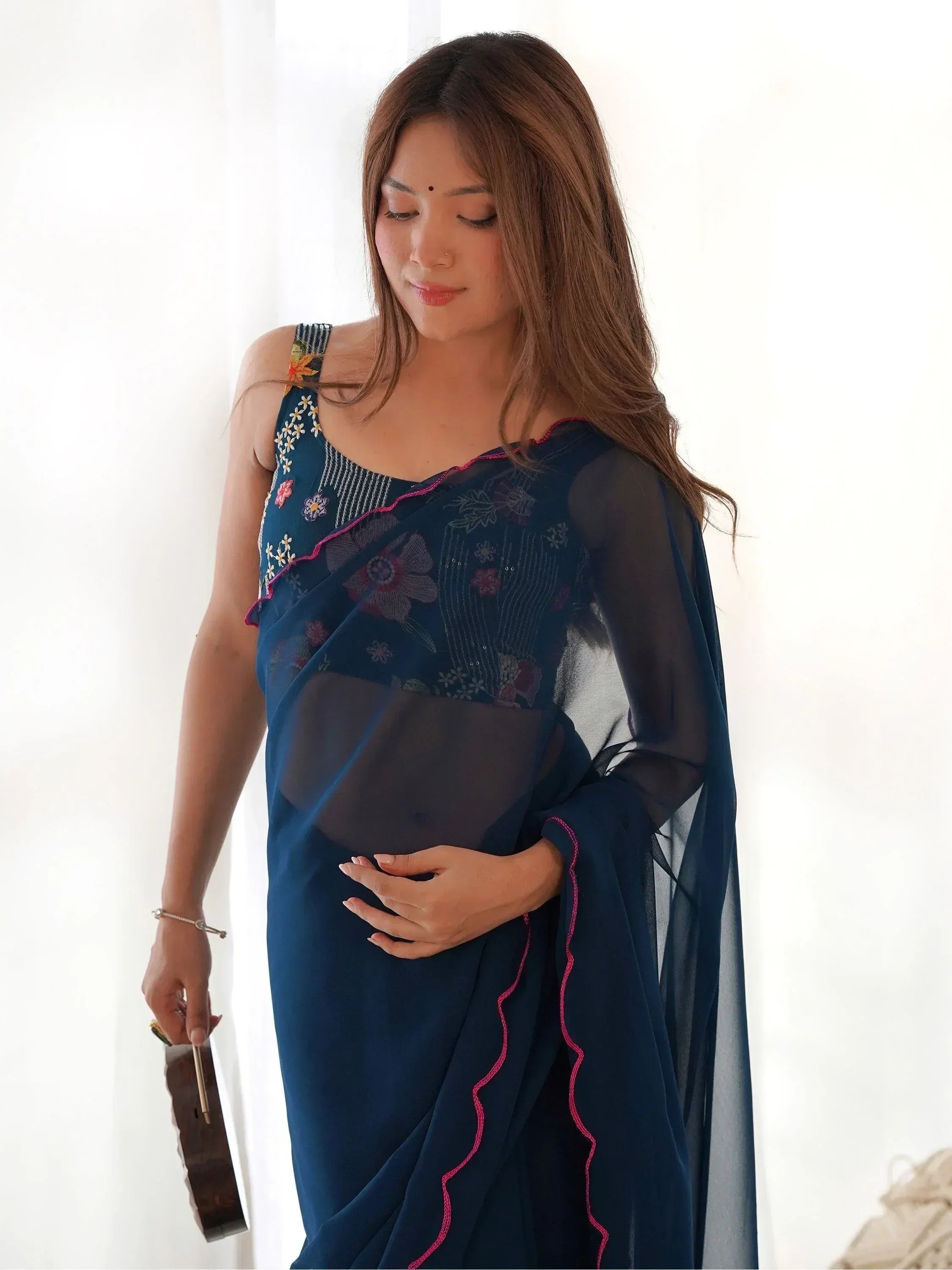 Pregnant woman in navy blue embroidered saree with floral design and sheer overlay, holding belly