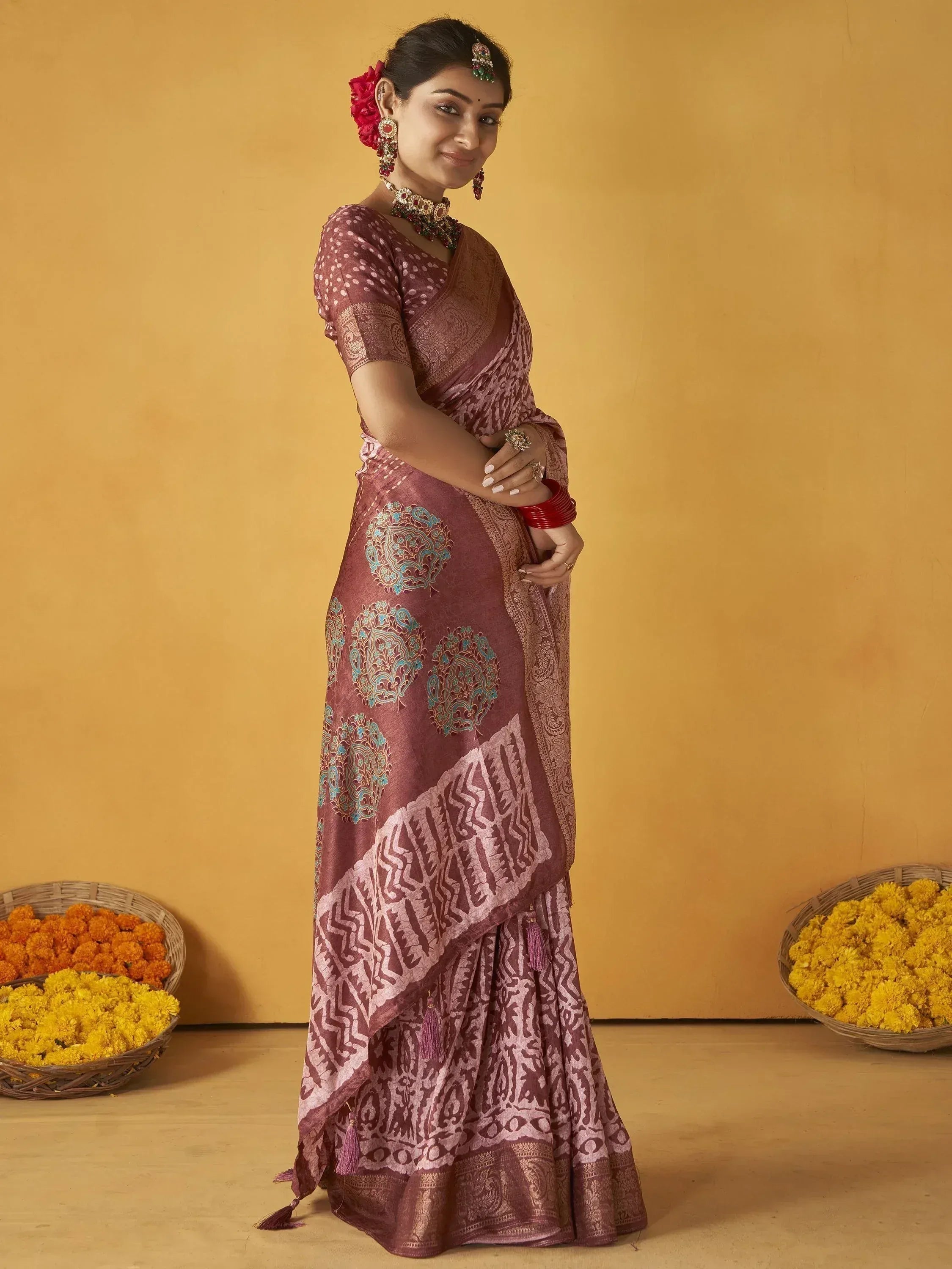 Woman in maroon ethnic saree with blue motifs, traditional jewelry, and floral baskets, perfect for Indian occasions.