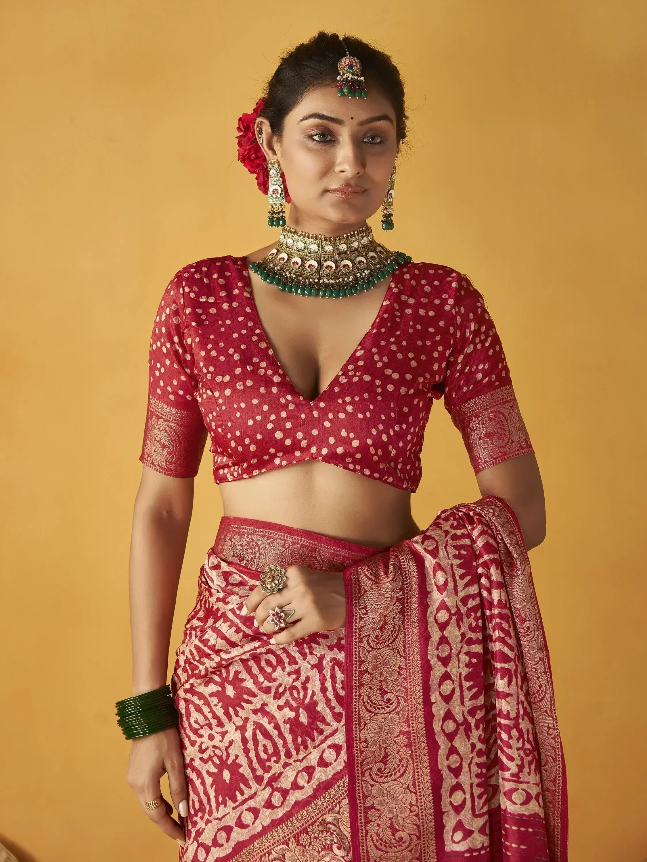Woman in red ethnic saree with polka dot blouse, traditional jewelry, and floral hair accessory
