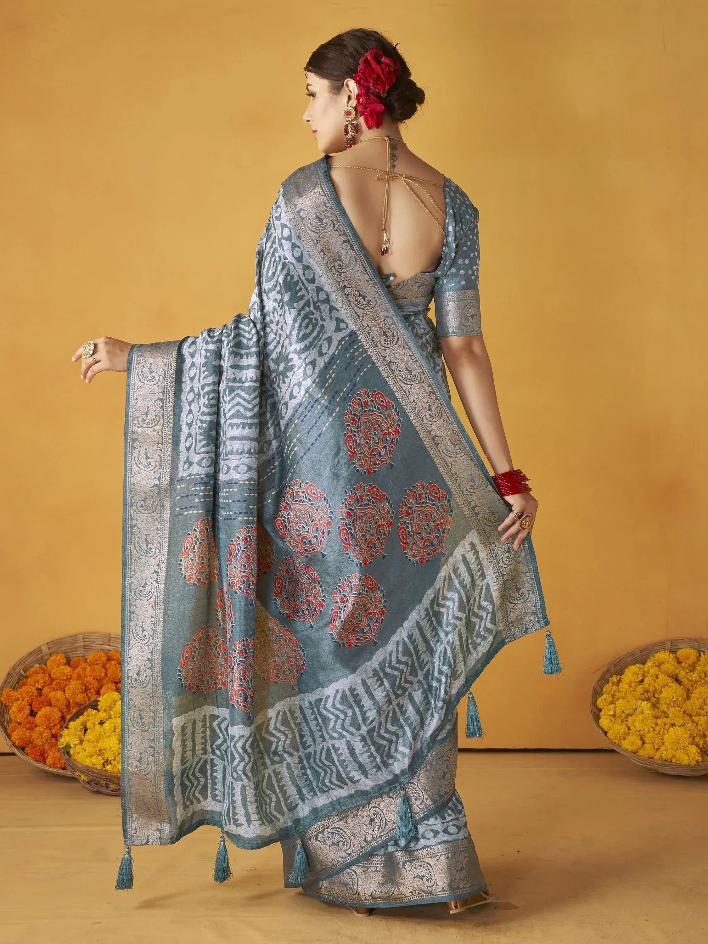 Blue printed saree with red motifs, tassels, and backless blouse, styled with flowers and marigolds