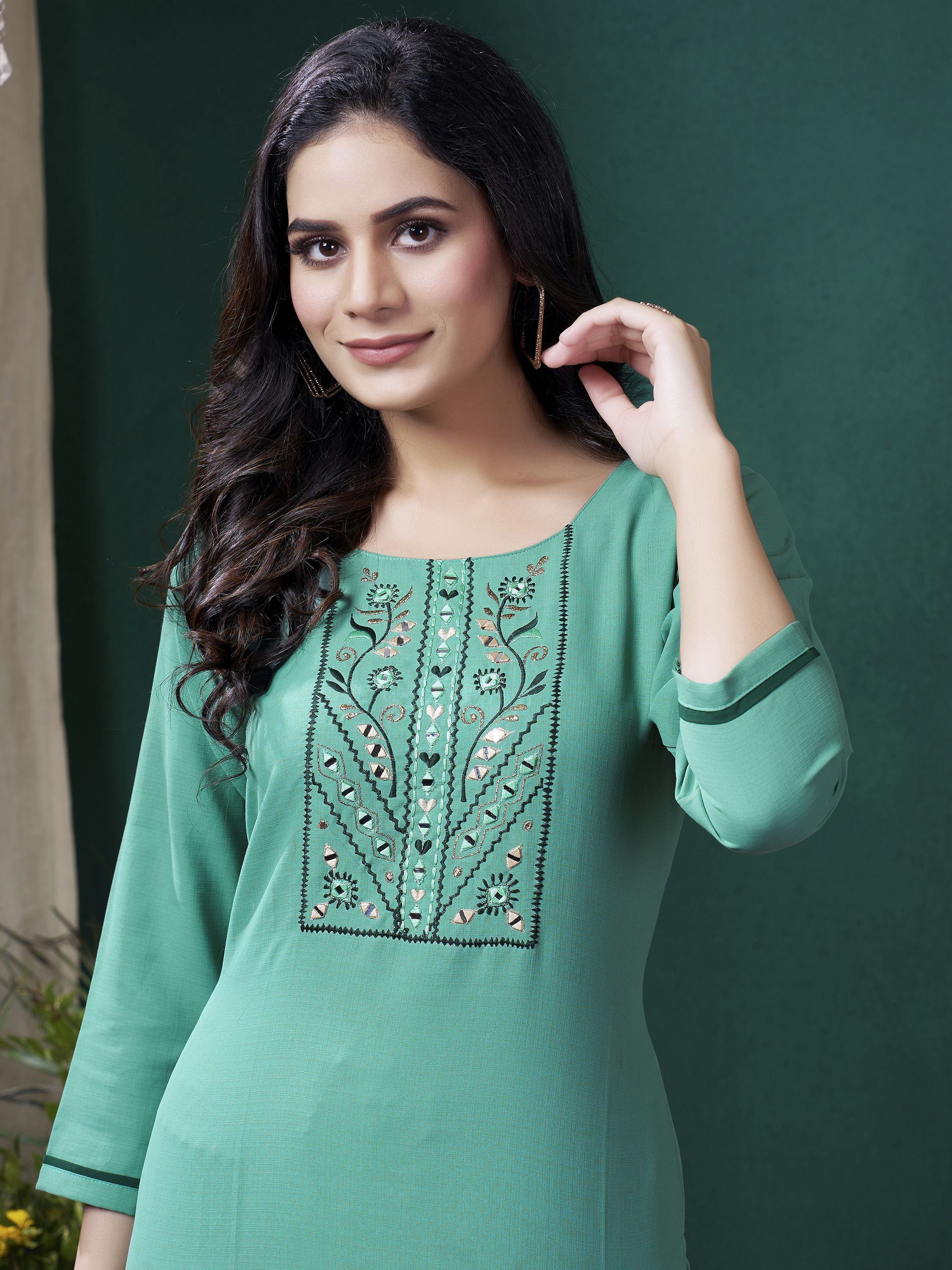 Woman in green ethnic kurti with mirror work embroidery, posing against solid backdrop