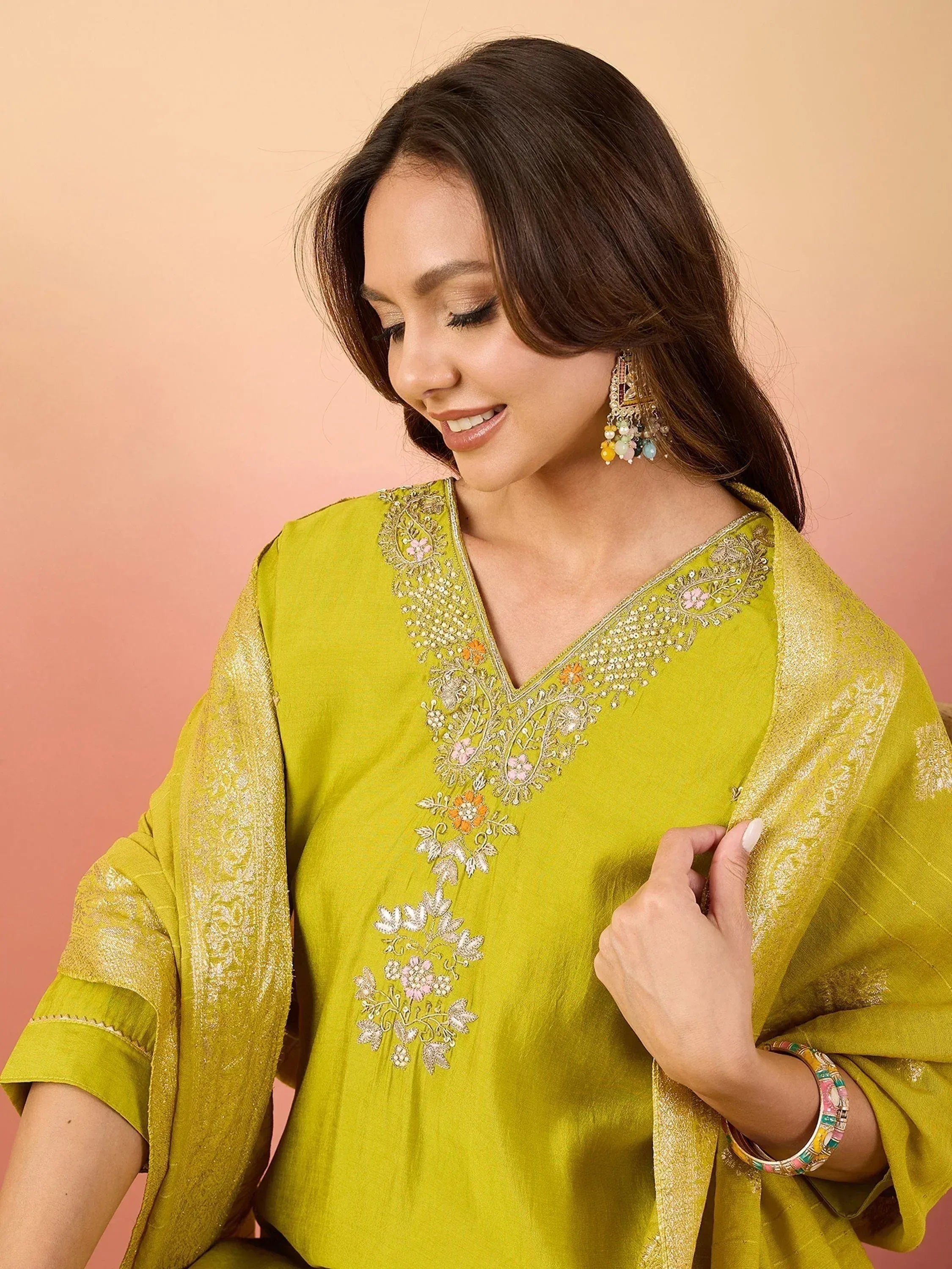 Woman in vibrant green embroidered ethnic kurti with floral detailing and gold trim, paired with statement earrings.