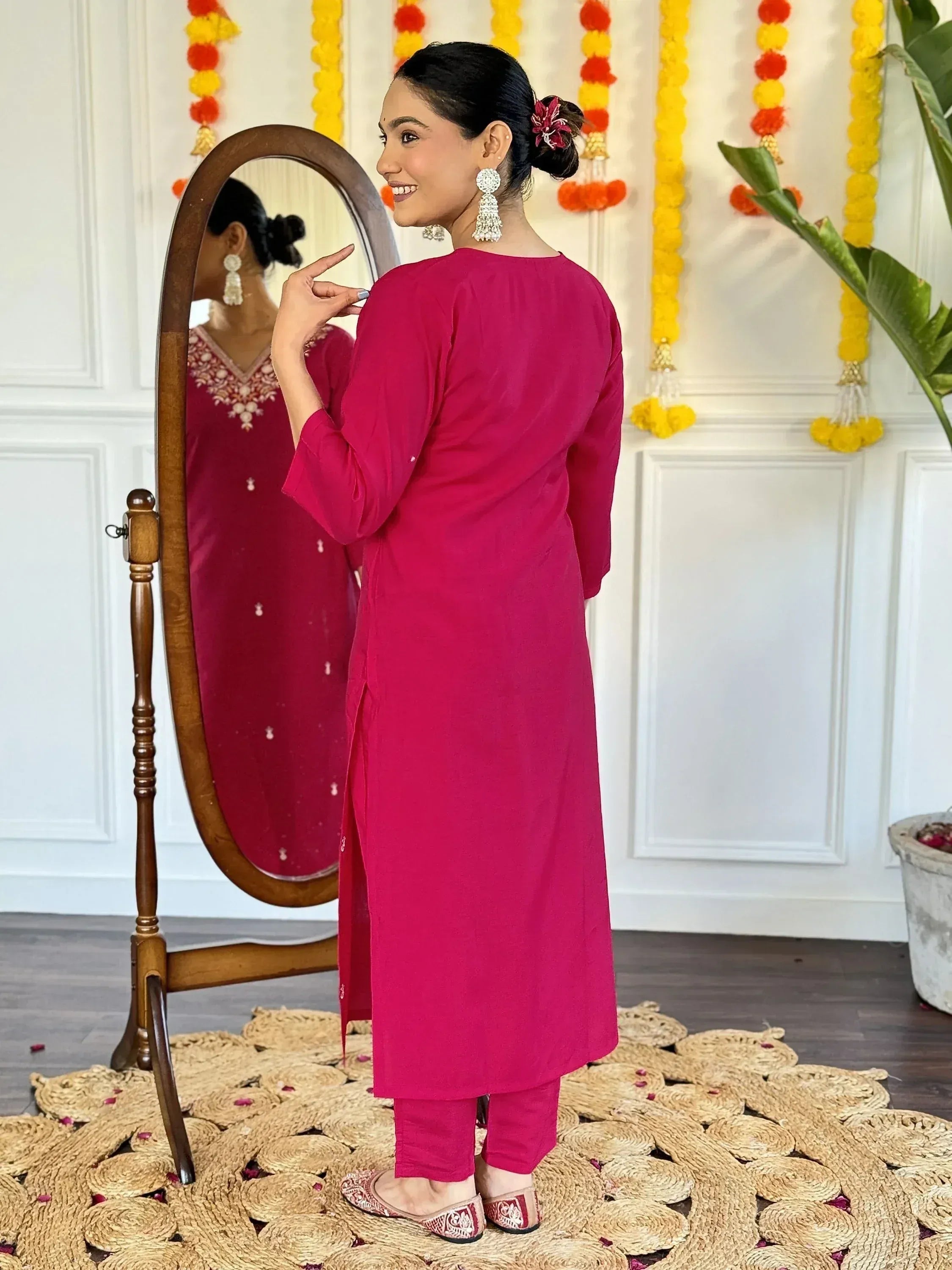 Woman in vibrant pink ethnic kurta with mirror reflection, festive decor, and traditional jewelry