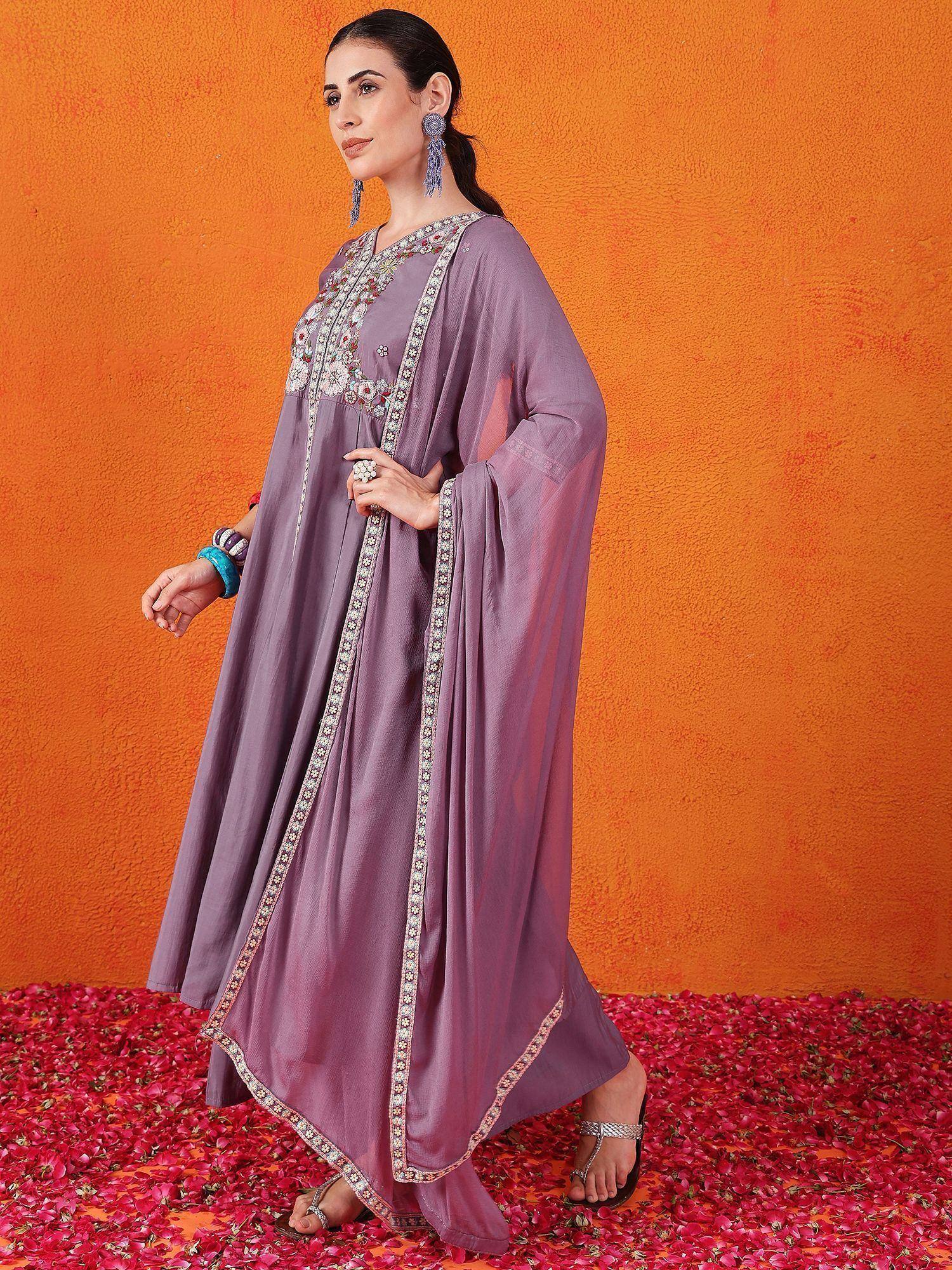 Purple embroidered ethnic gown with floral detailing, paired with statement earrings and sandals, perfect for festive occasions.