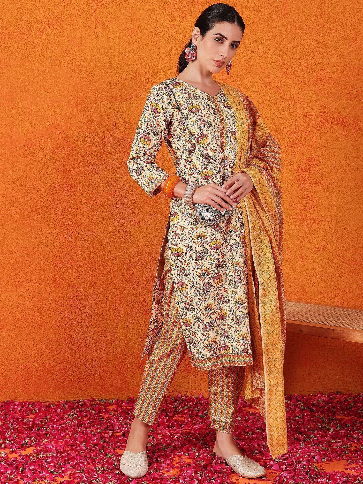 Woman in floral printed salwar kameez with yellow dupatta, posing on rose petals, orange background