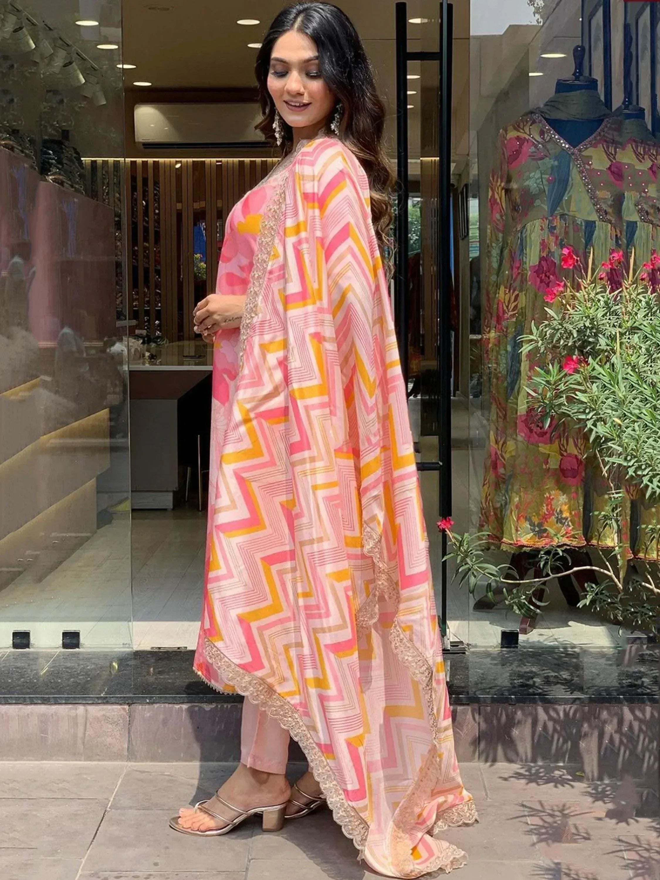 Woman in pink and yellow geometric print ethnic gown with lace trim, perfect for festive occasions.