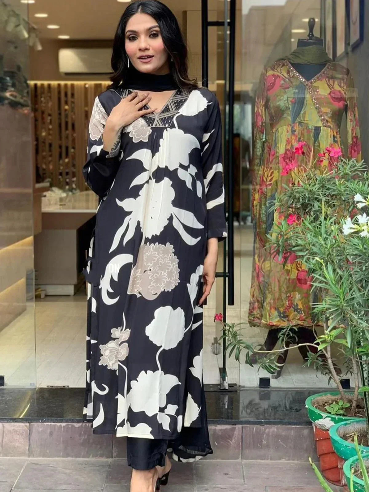 Woman wearing a black floral printed kurta with beige and white patterns, standing at store entrance.