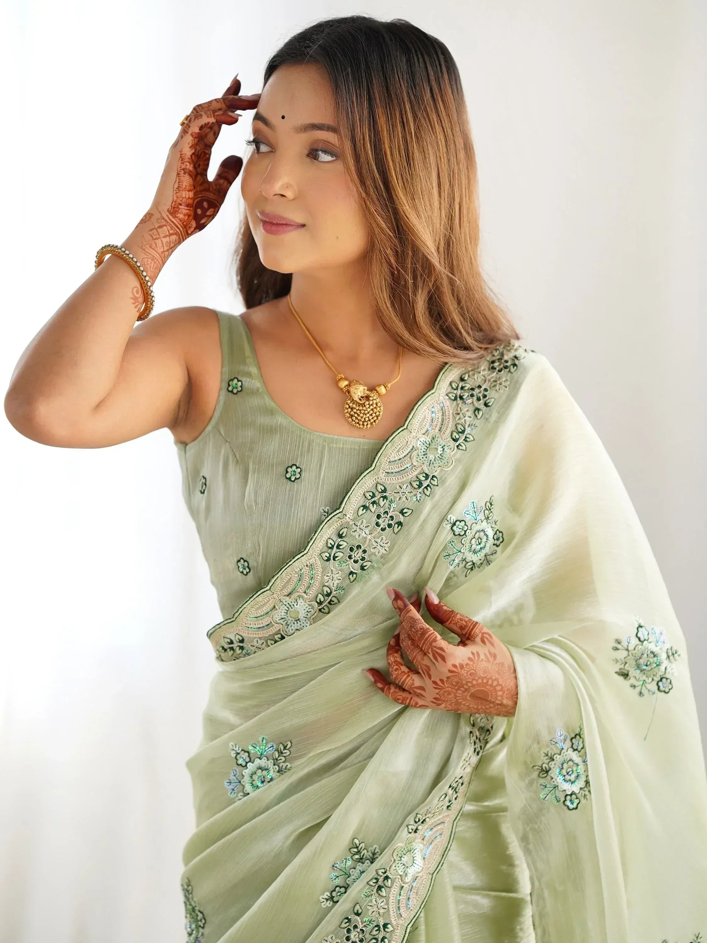Woman in light green embroidered saree with floral details and henna hands, styled for ethnic occasions.