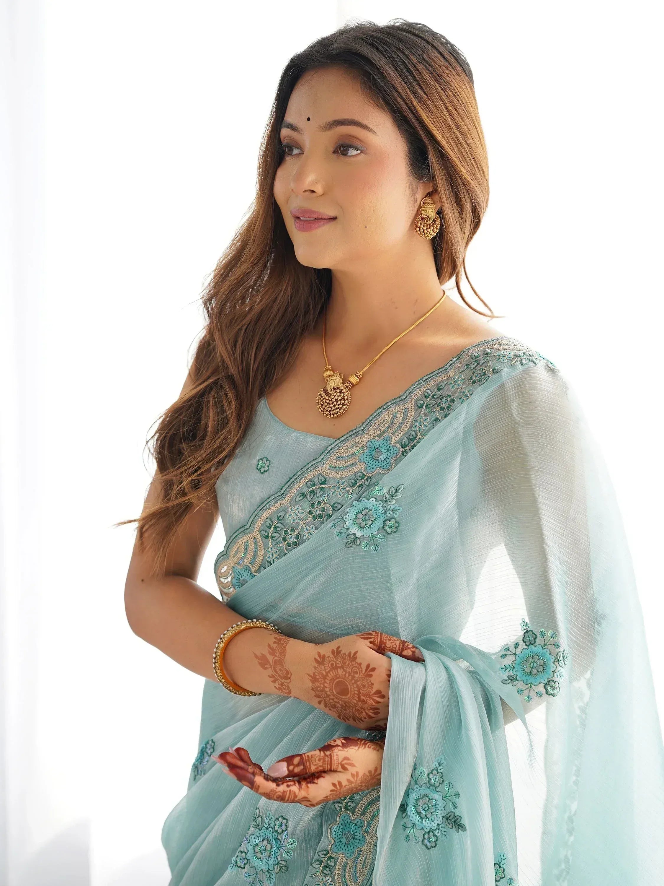 Woman in light blue embroidered saree with gold jewelry and henna hands, Indian ethnic wear