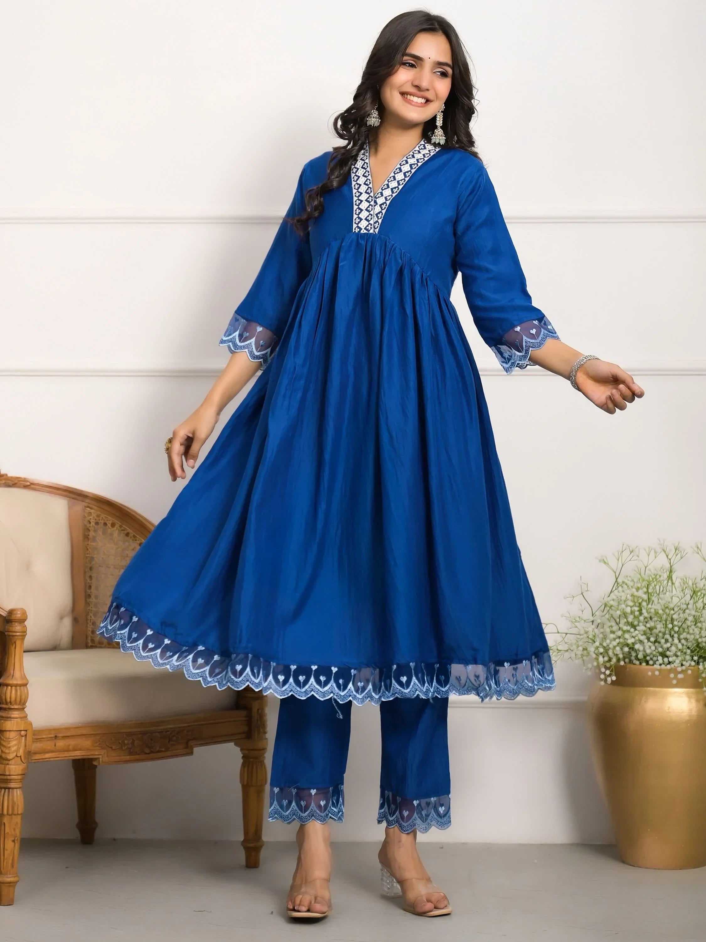Woman wearing blue embroidered ethnic kurti with matching pants, standing indoors