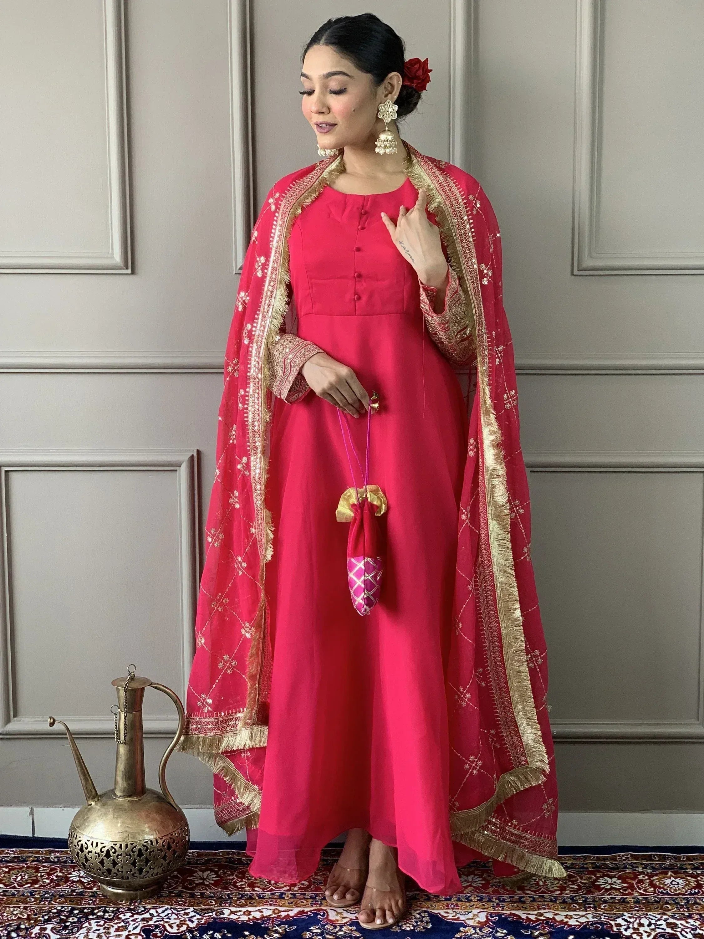 Woman in vibrant pink Indian ethnic gown with gold embroidery, matching dupatta, and traditional jewelry