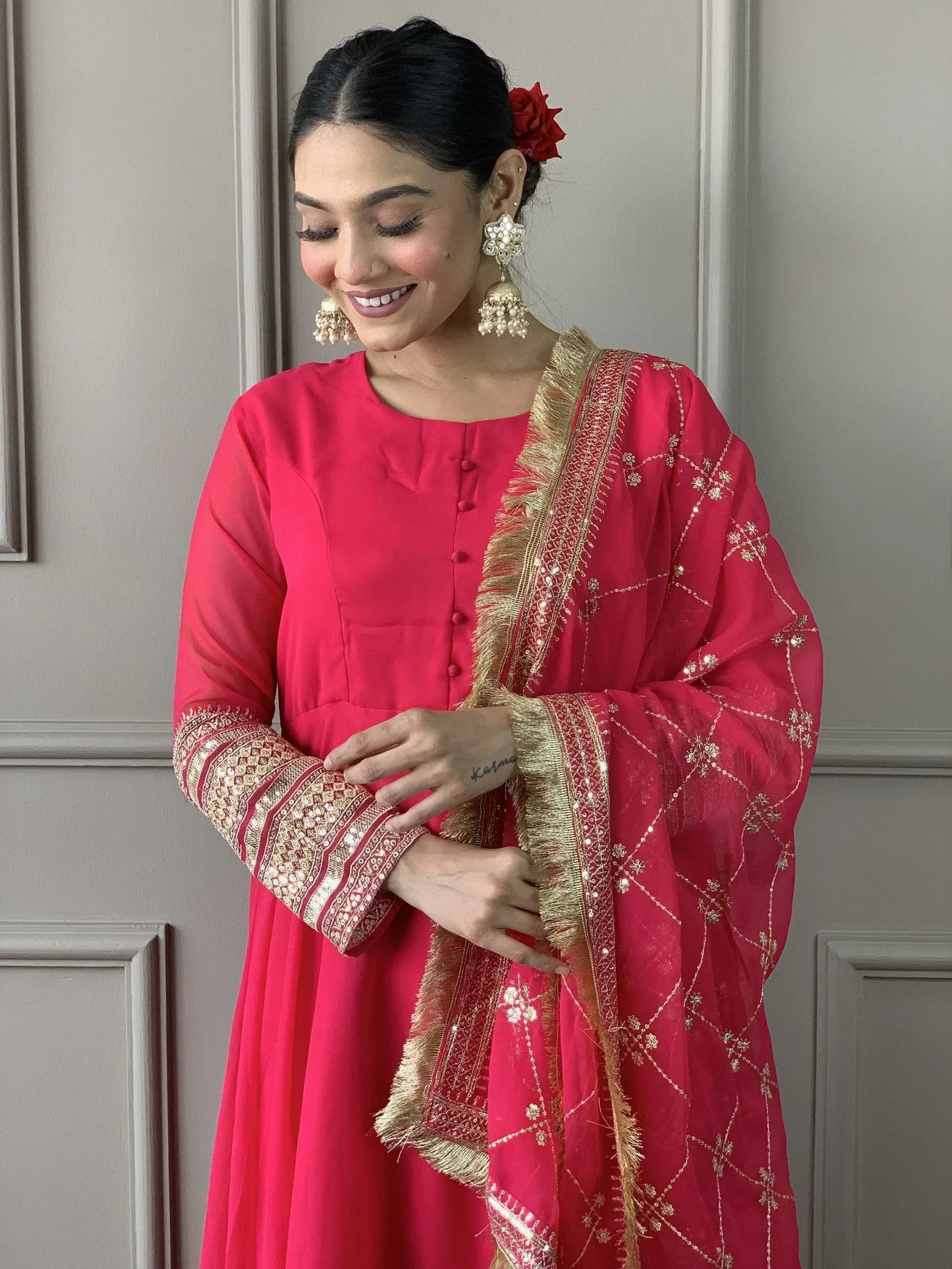 Pink Indian ethnic salwar kameez with gold embroidery and dupatta, styled with jhumka earrings and red flower hair accessory