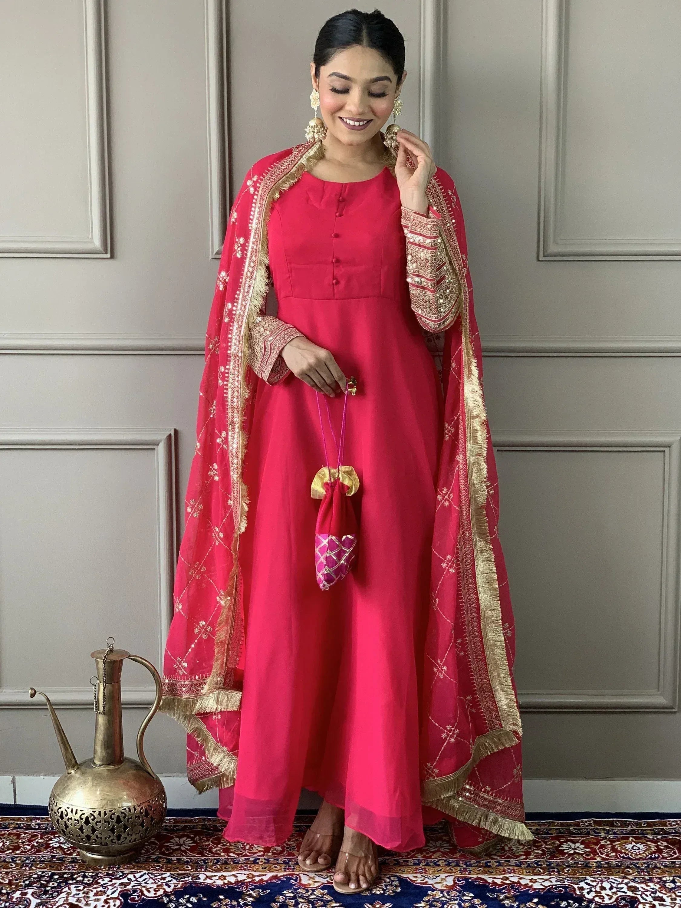Woman in vibrant pink Indian ethnic anarkali with gold embroidery, dupatta, and matching potli bag