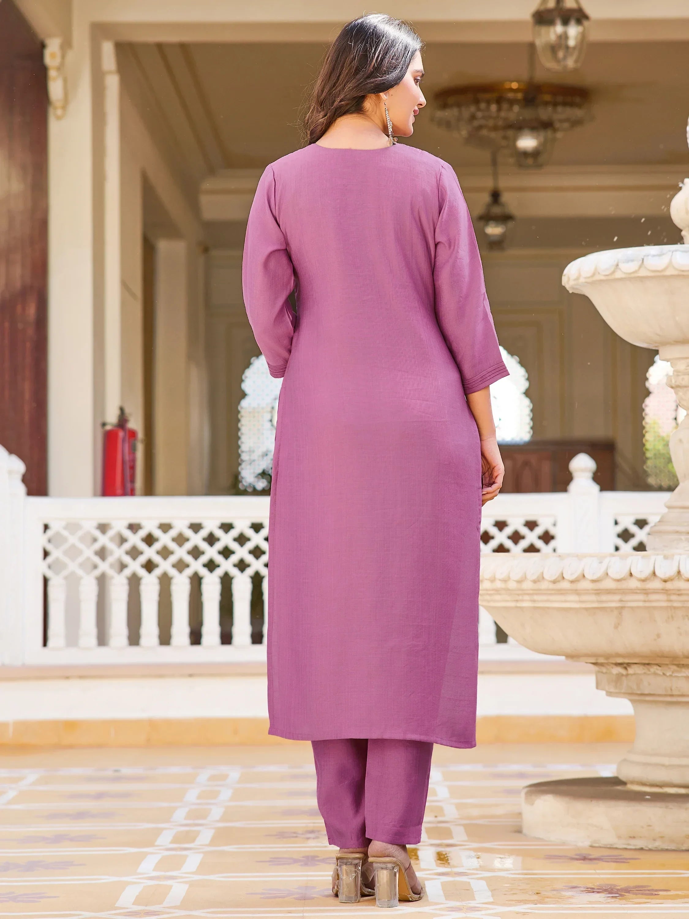 Woman wearing mauve straight kurta set with pants, standing outdoors by a white fountain