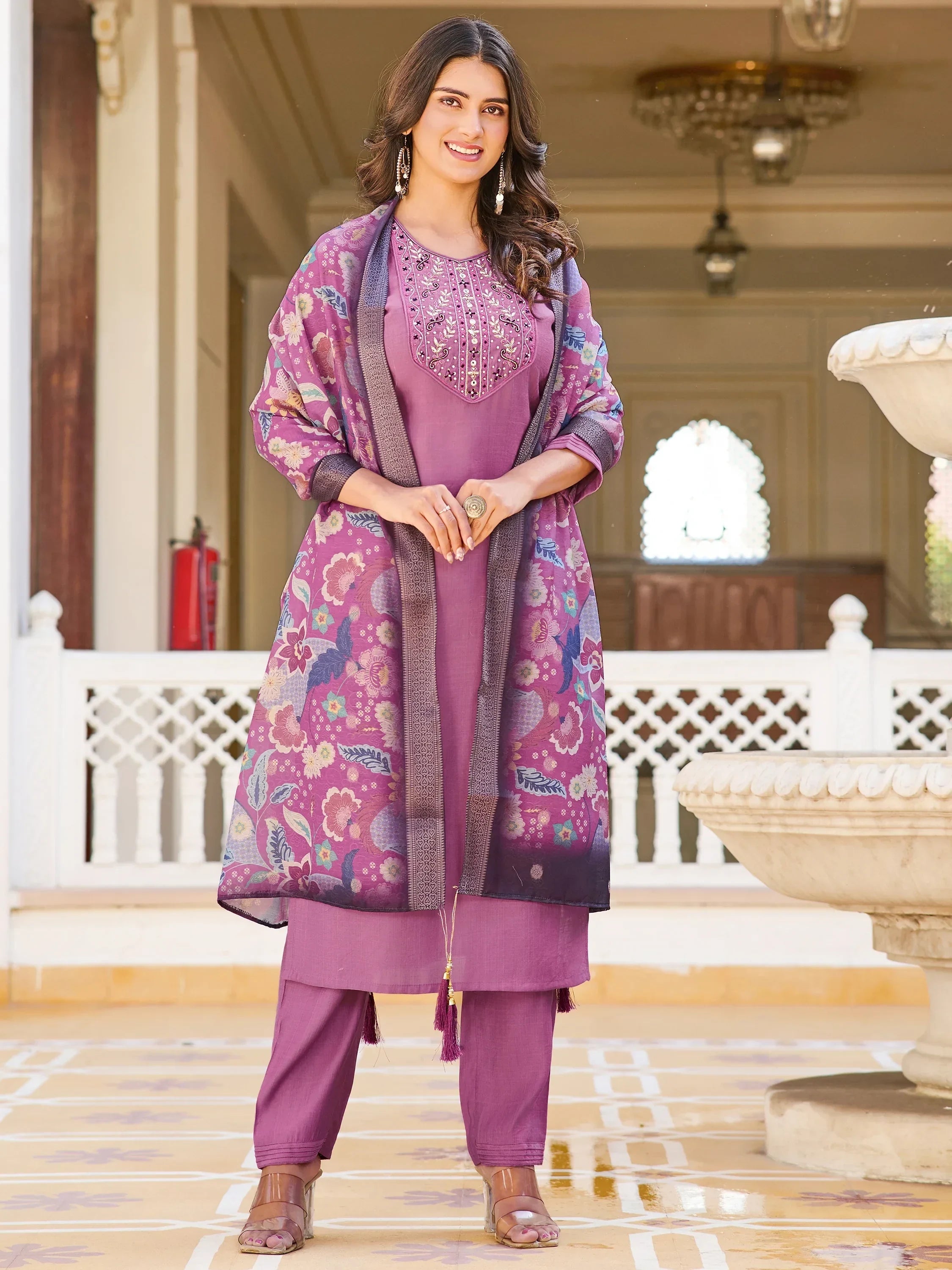 Woman in mauve embroidered salwar kameez with floral dupatta, standing in courtyard