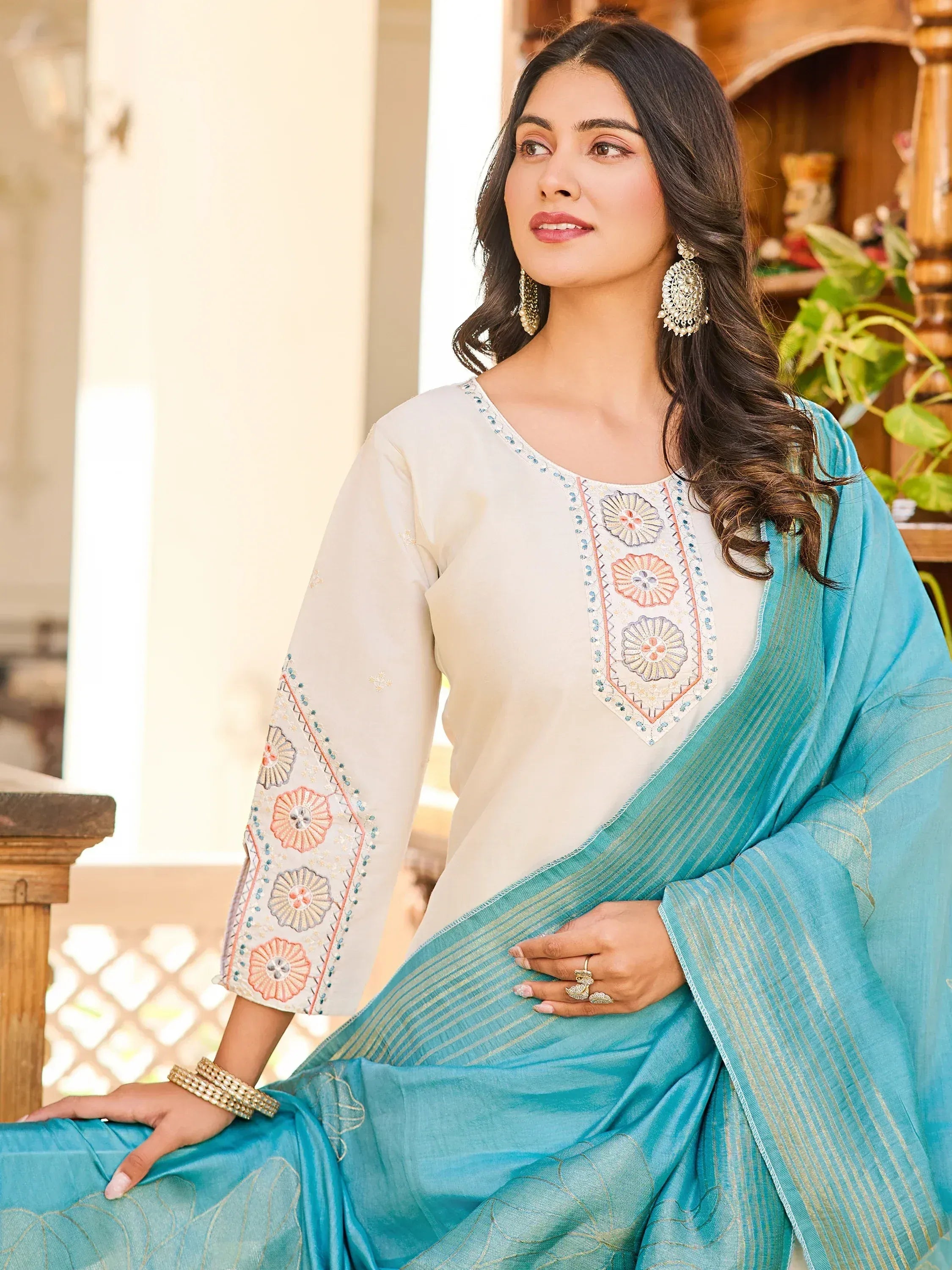 Woman in elegant Indian ethnic wear with floral embroidery, cream top and turquoise saree, perfect for festive occasions.