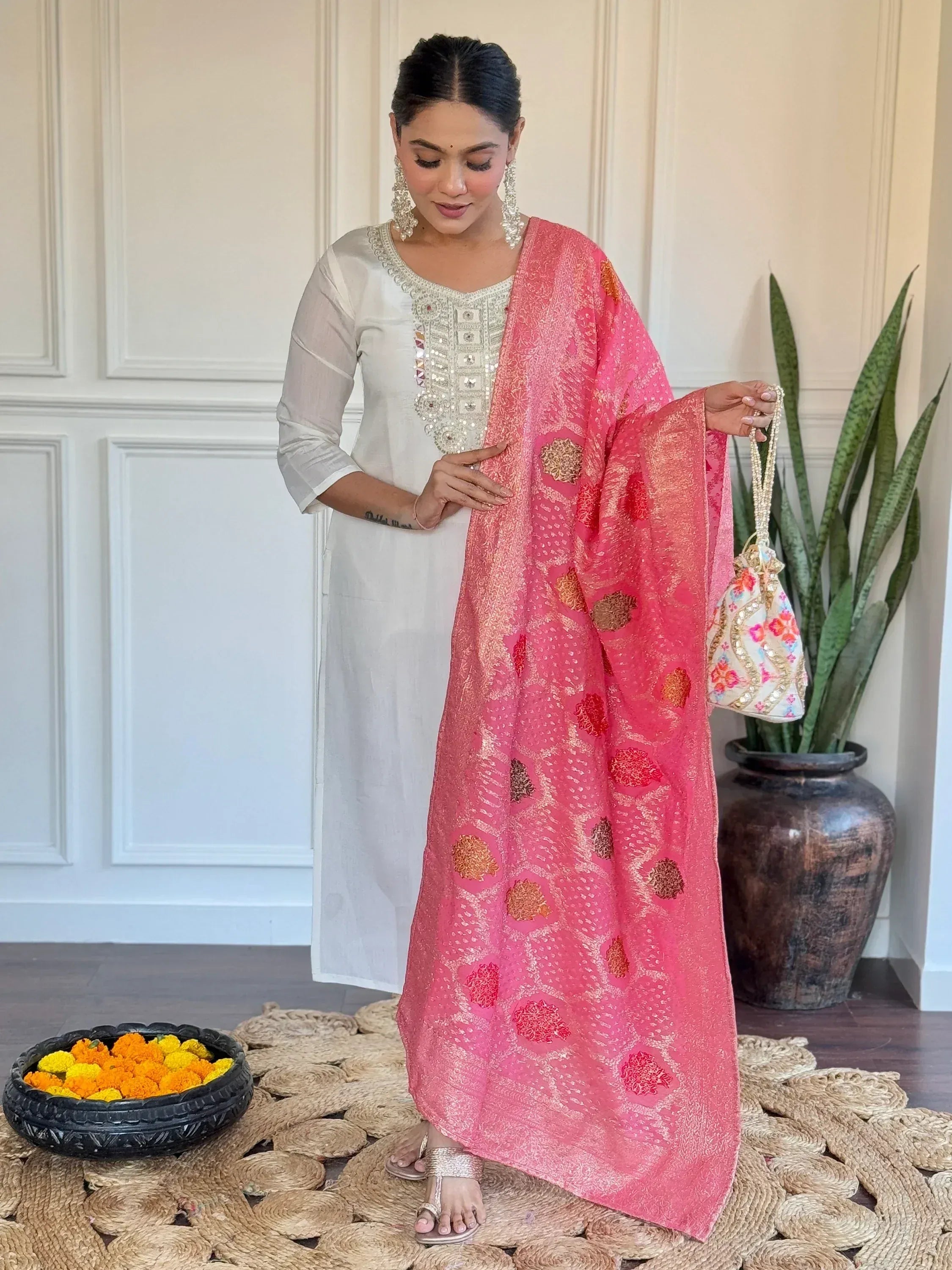 Woman in white embroidered kurta with pink floral dupatta, holding potli bag, festive ethnic wear
