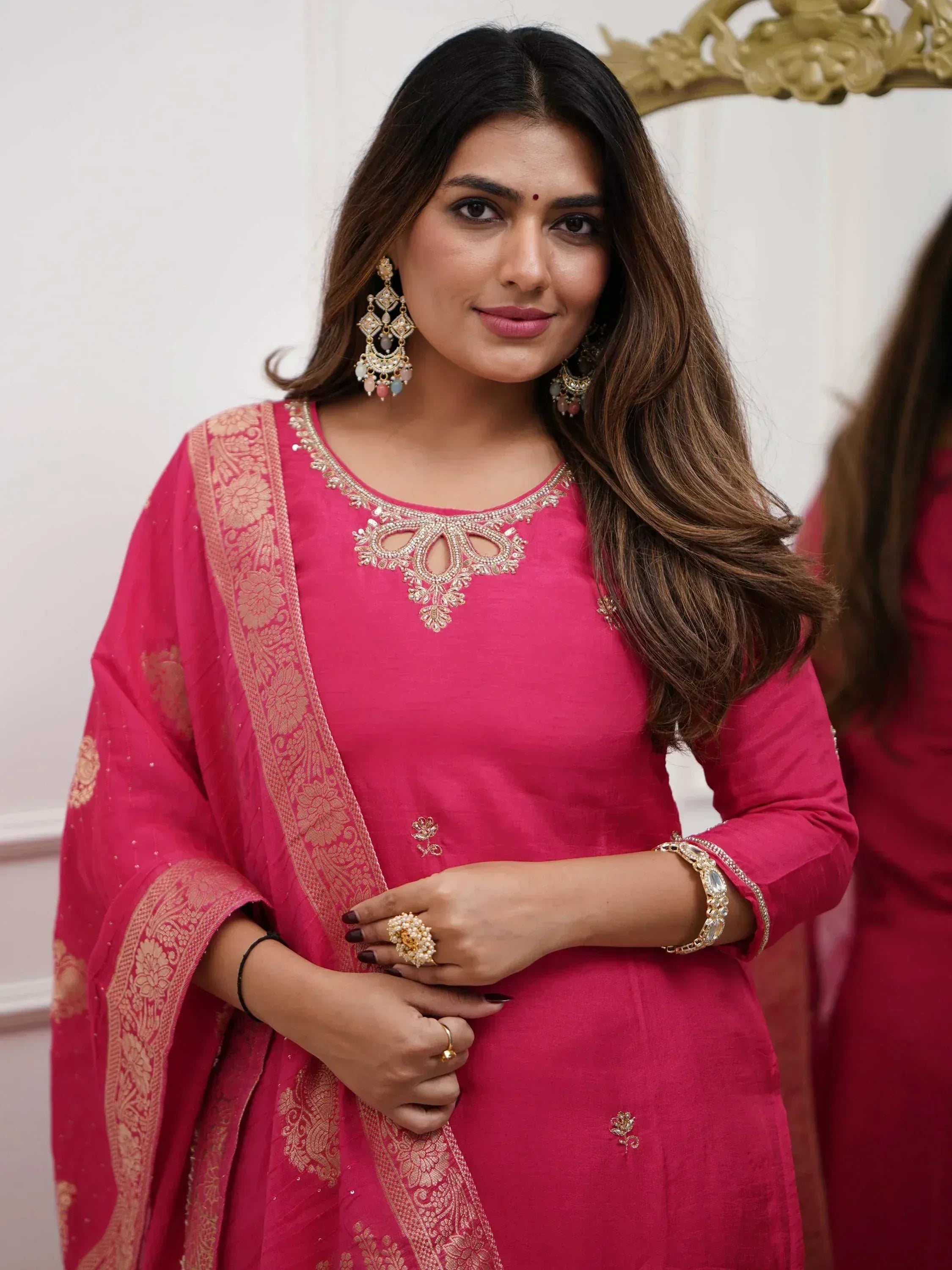 Woman in pink embroidered Indian ethnic wear with gold detailing and traditional jewelry