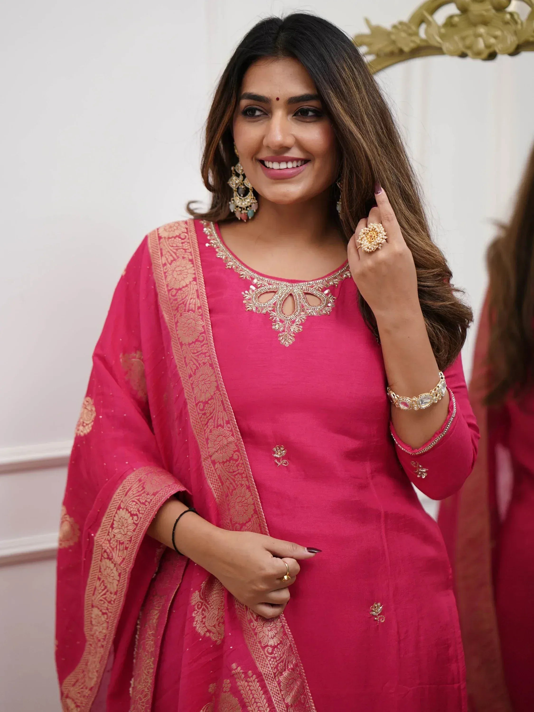 Woman in pink embroidered salwar kameez with gold detailing and matching dupatta, styled with traditional jewelry