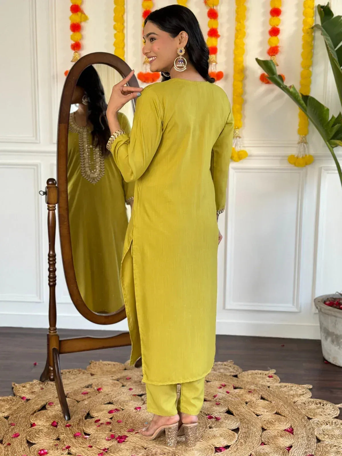 Woman in mustard yellow ethnic kurta set with mirror reflection, floral decor, and jute rug