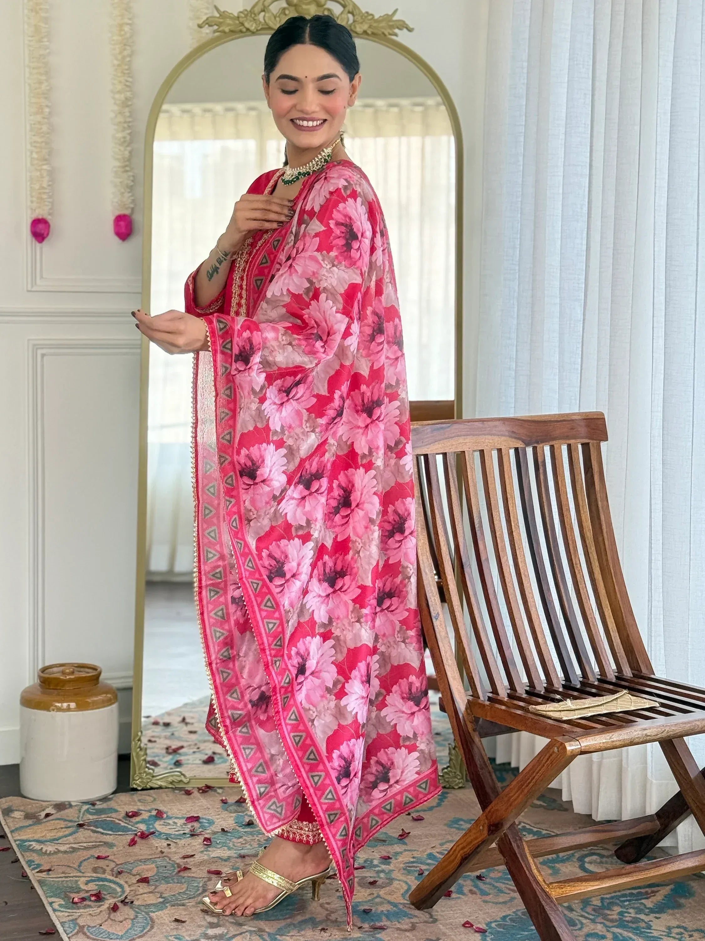Woman in pink floral ethnic saree with gold heels, styled in elegant indoor setting