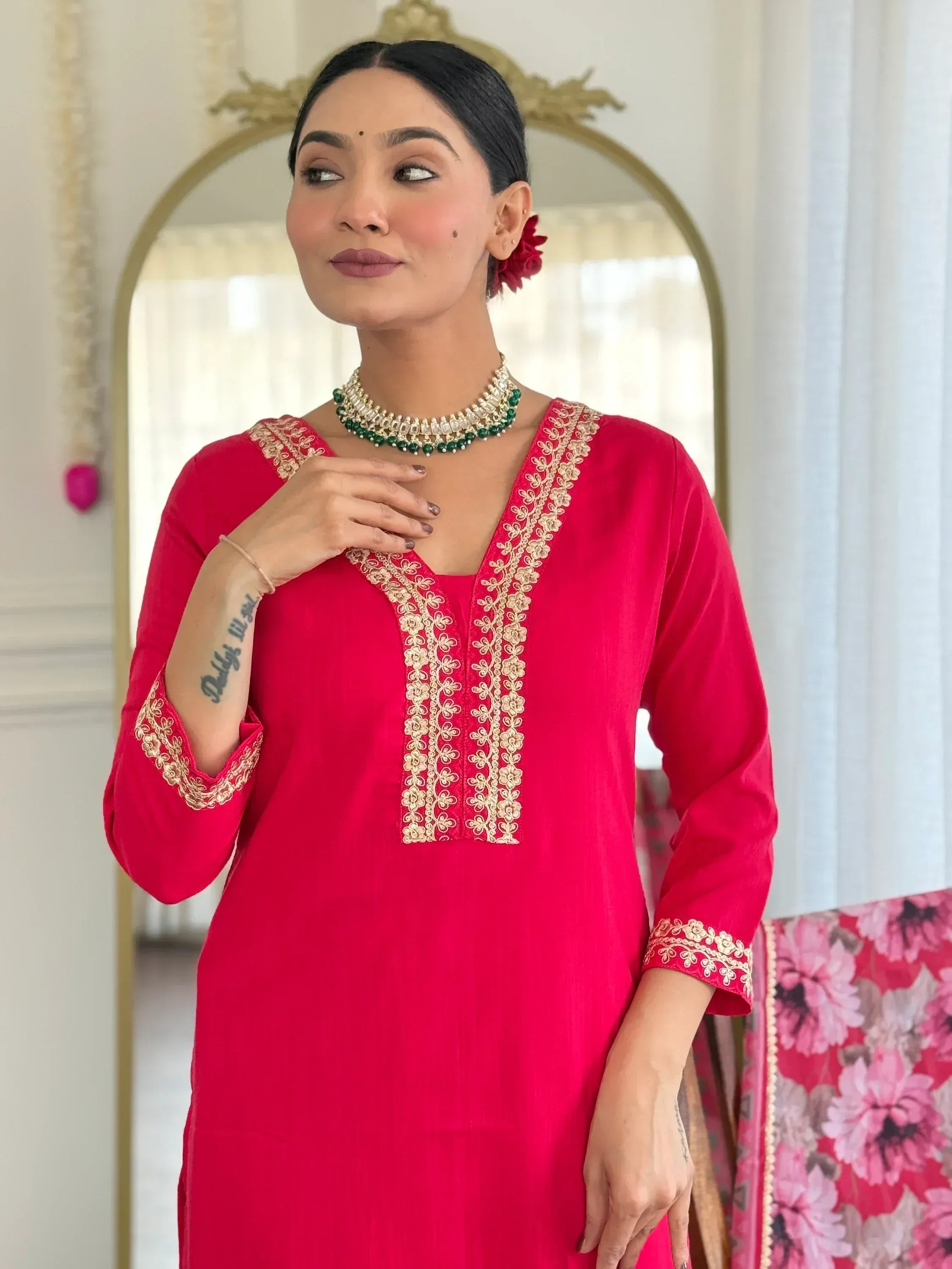 Woman in red embroidered kurta with gold detailing, paired with green necklace, ideal for ethnic wear.