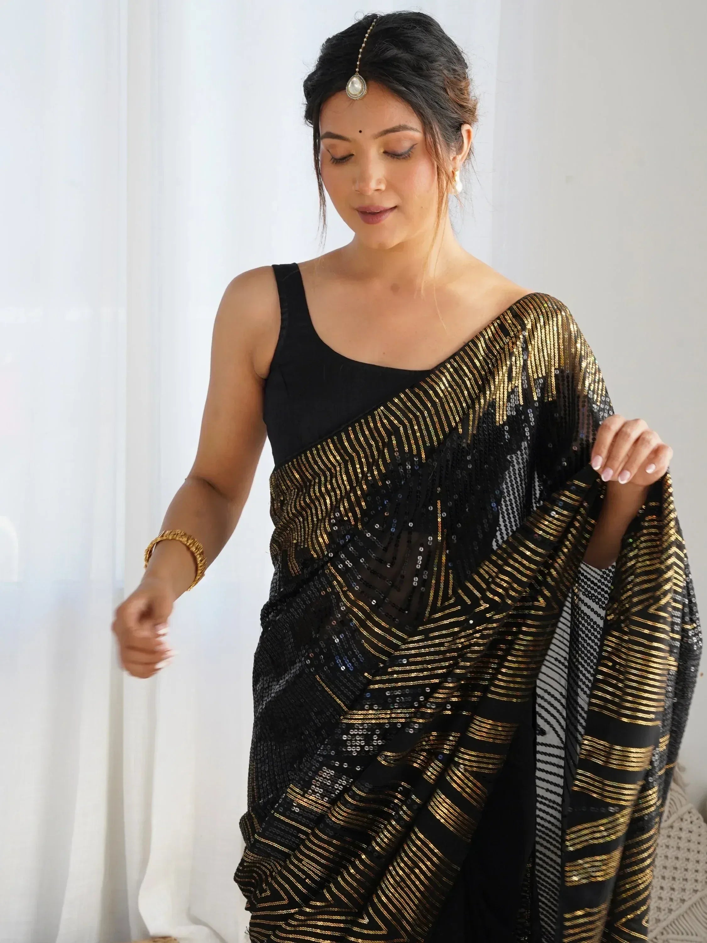 Black and gold sequin saree with geometric pattern, paired with black blouse and traditional jewelry