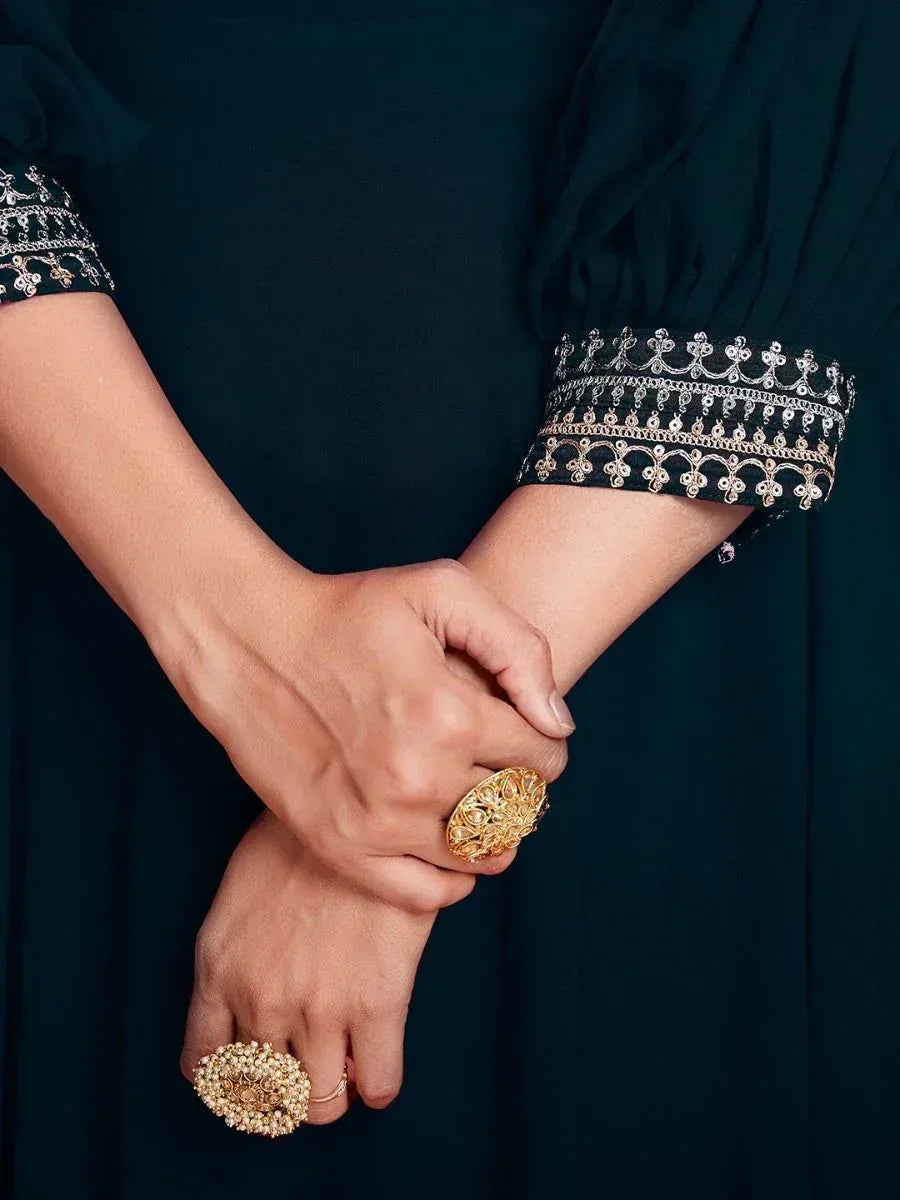 Elegant dark green ethnic gown with intricate gold embroidery and statement rings
