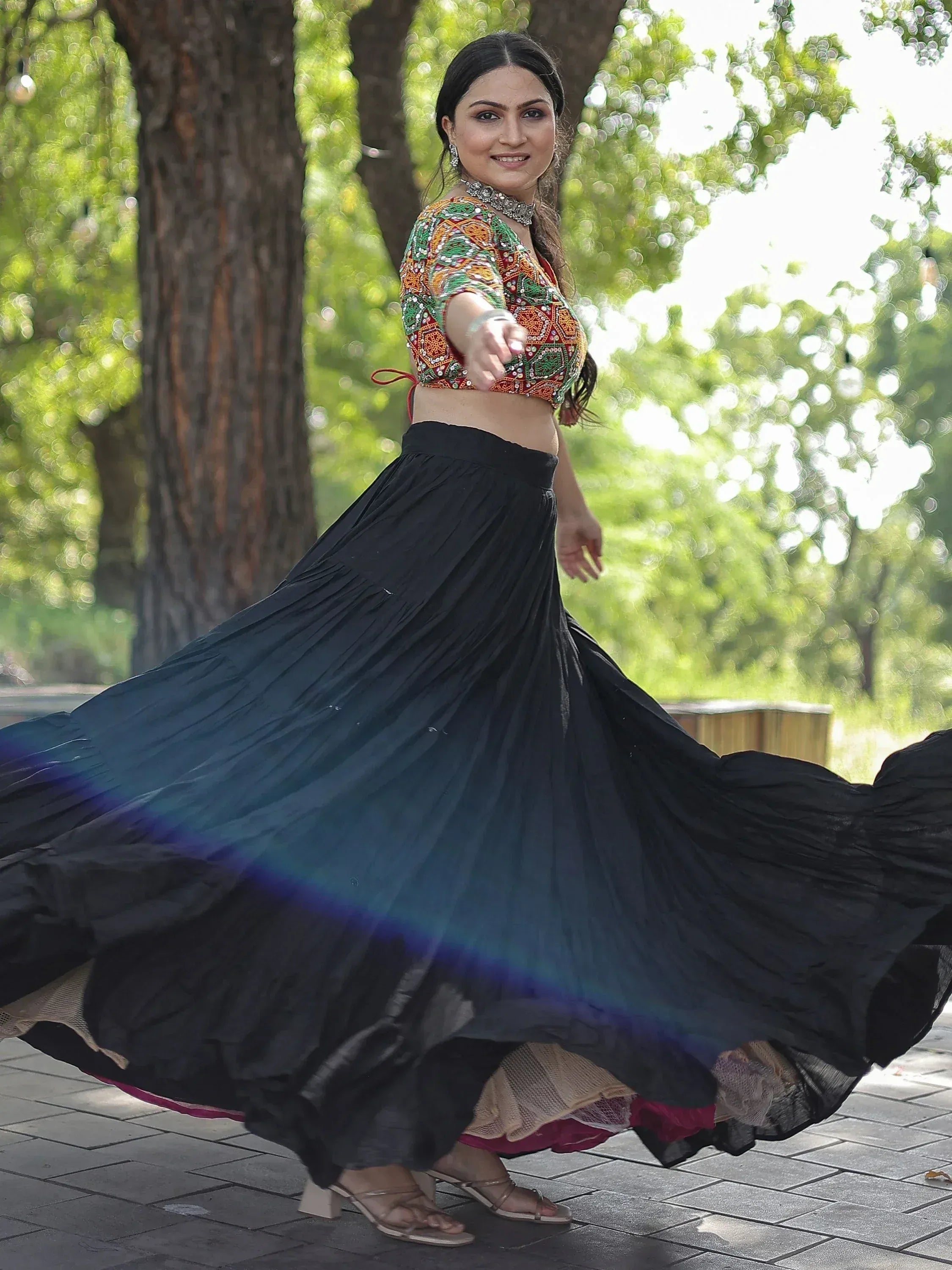 Woman twirling in colorful embroidered crop top and black pleated skirt, Indian ethnic wear