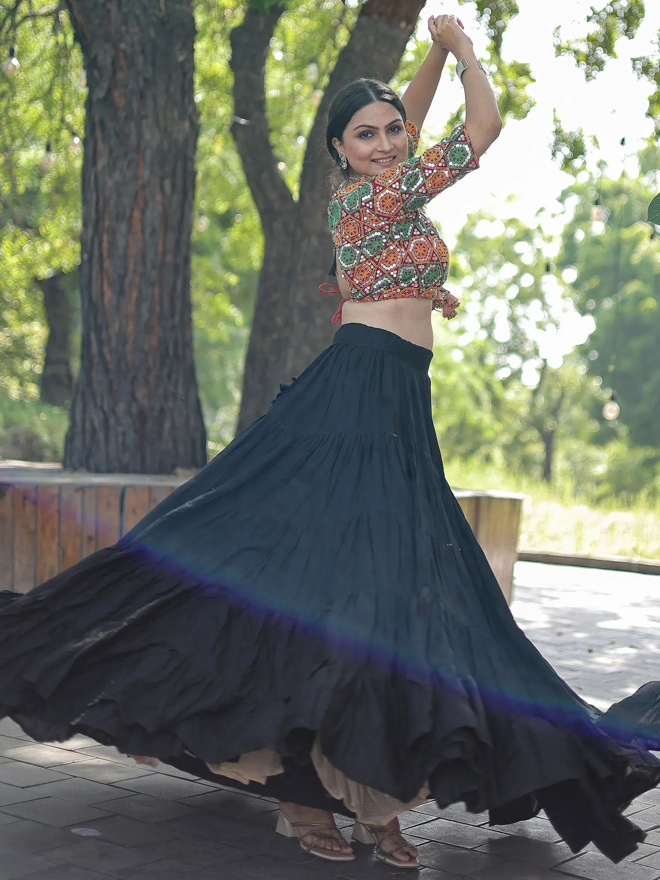 Woman in colorful embroidered crop top and flowing black skirt, dancing outdoors under trees