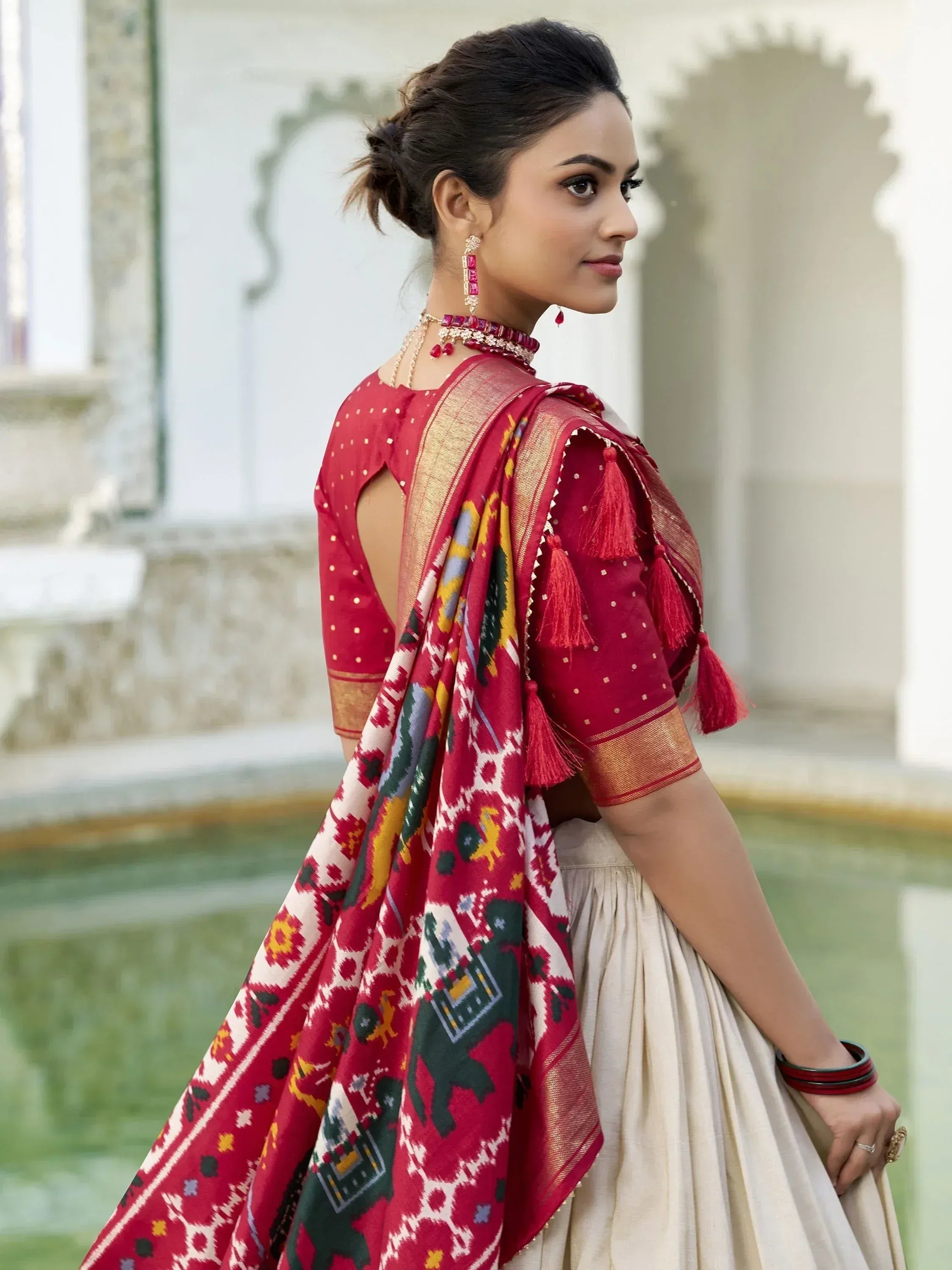 Woman in red ethnic lehenga choli with ikat dupatta, tassels, and gold trim, perfect for Indian weddings or festivals.
