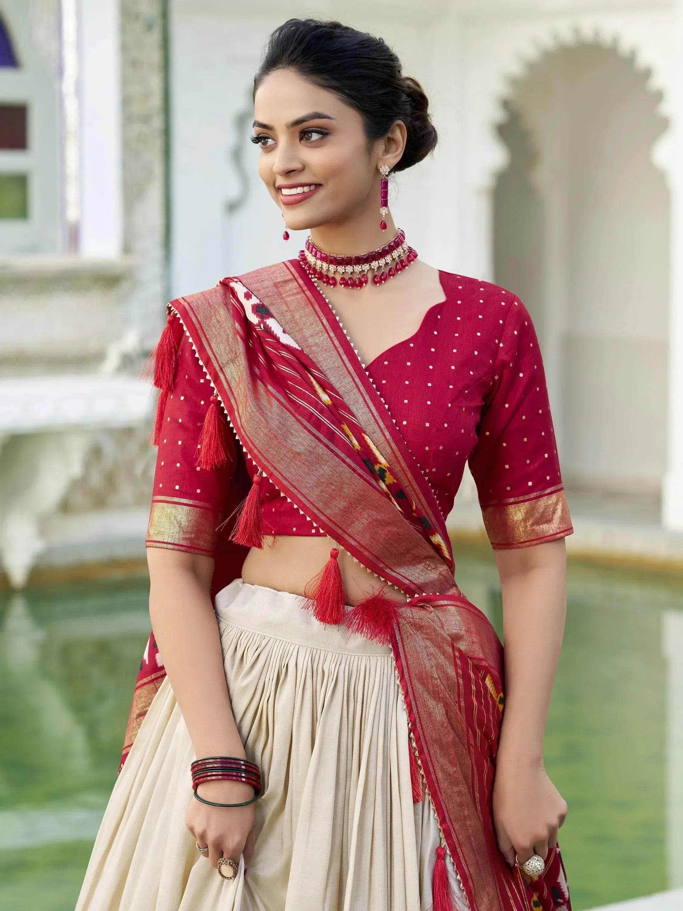 Red ethnic lehenga choli with tassels, paired with cream skirt and traditional jewelry for festive occasions