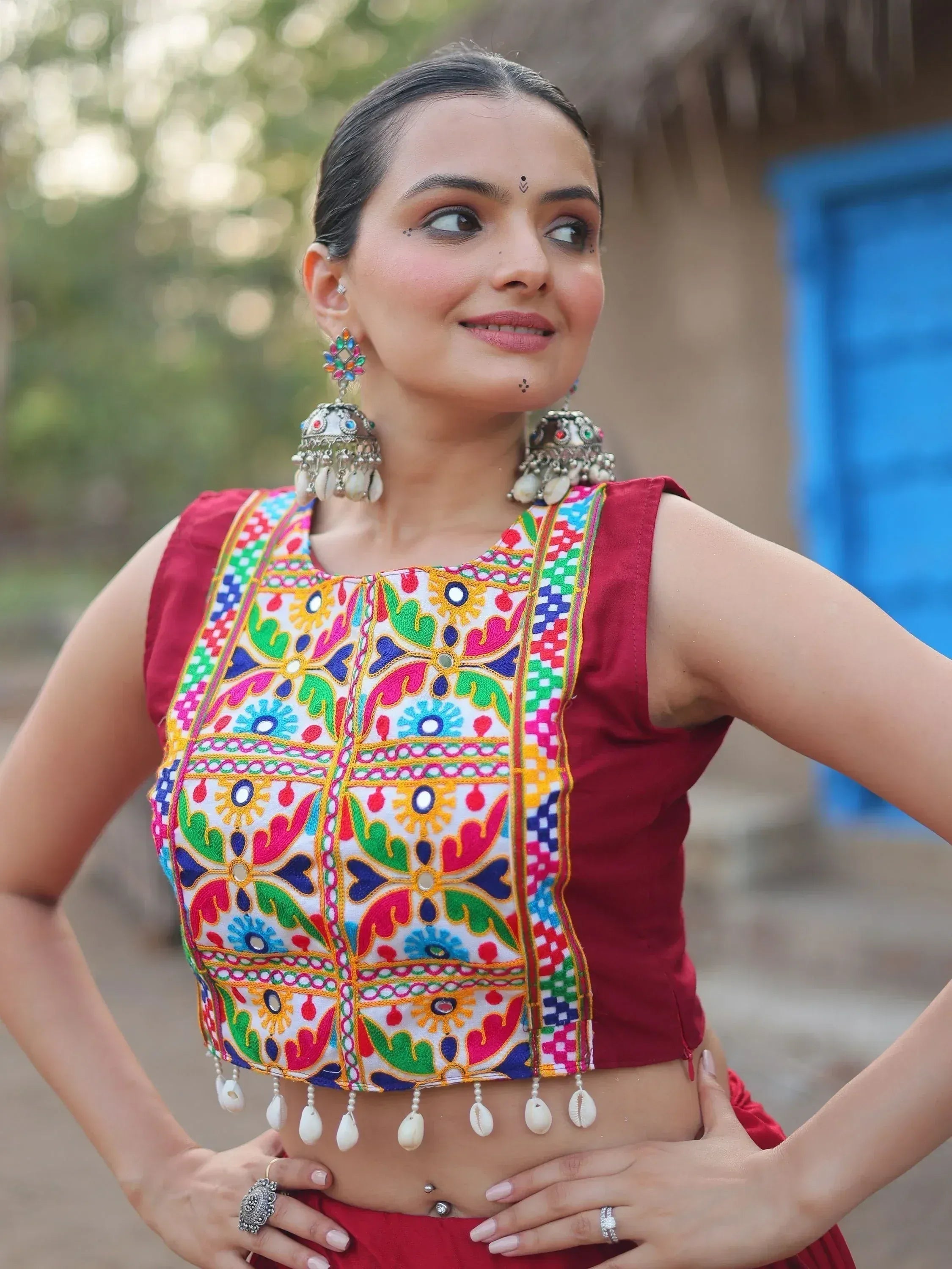 Woman in vibrant embroidered ethnic crop top with mirror work and shell tassels, paired with traditional jewelry