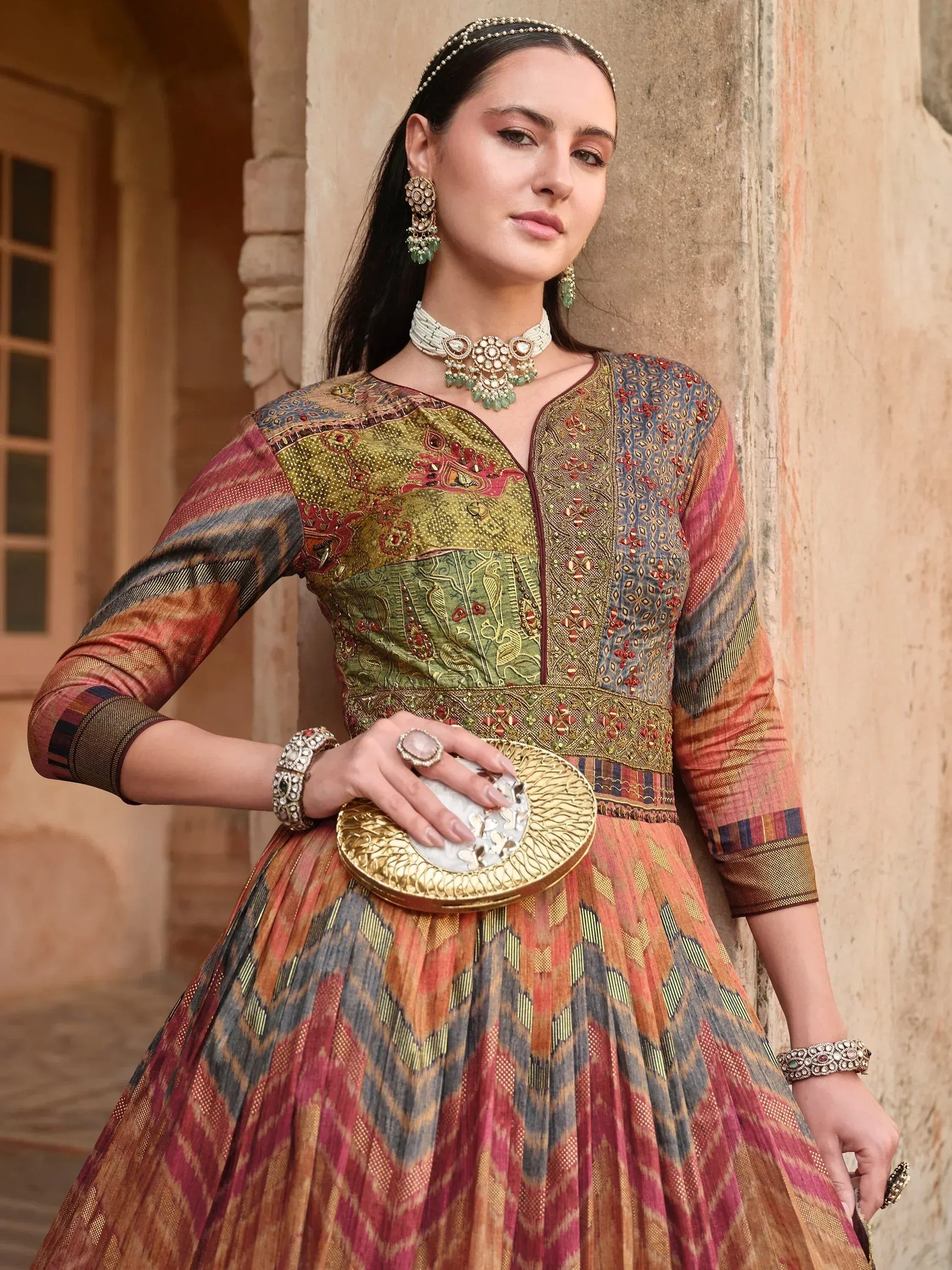 Woman in colorful Indian ethnic gown with intricate embroidery, traditional jewelry, and clutch, perfect for festive occasions.