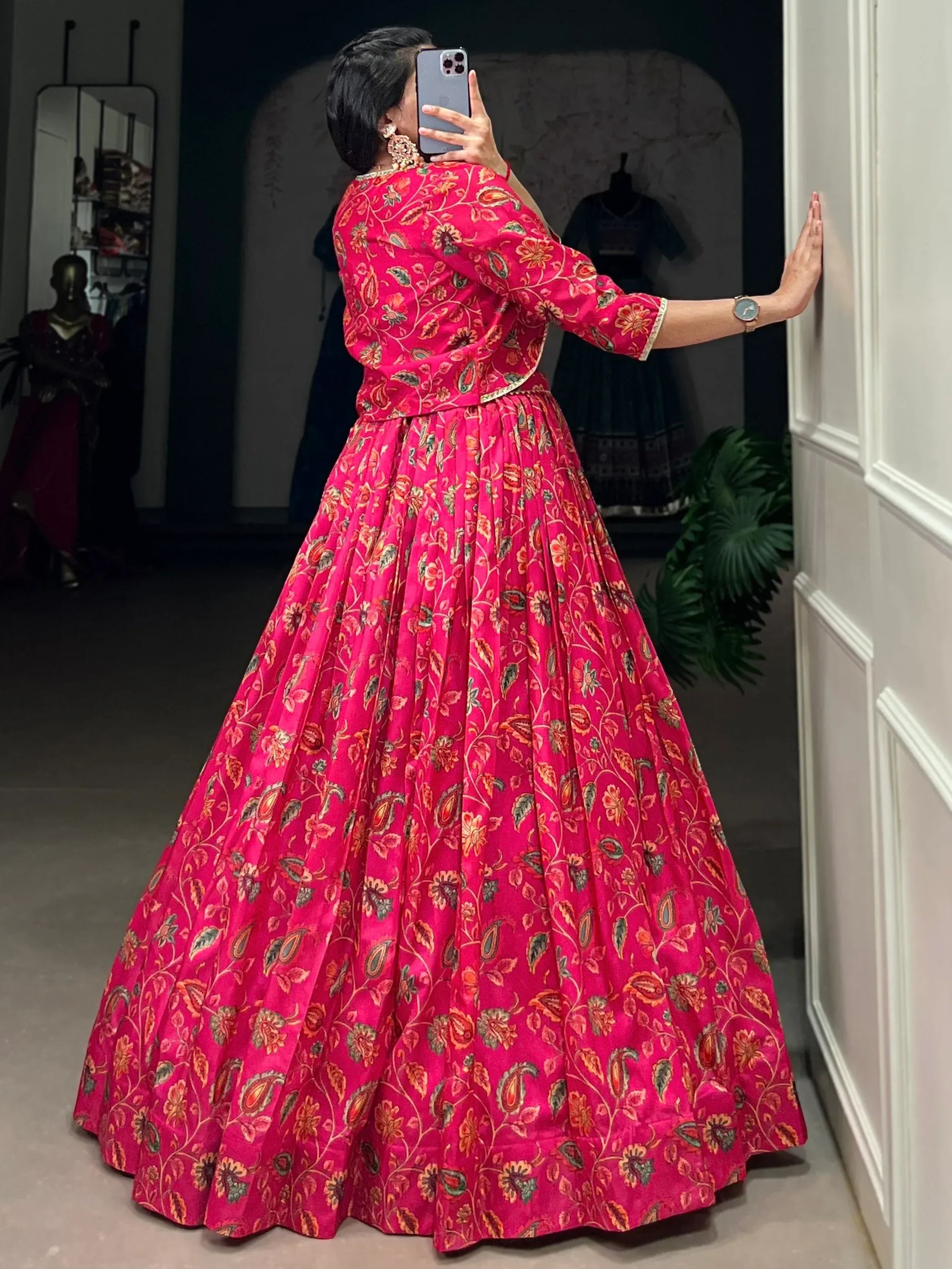 Woman in vibrant pink floral printed Indian ethnic gown taking mirror selfie, showcasing designer lehenga choli style