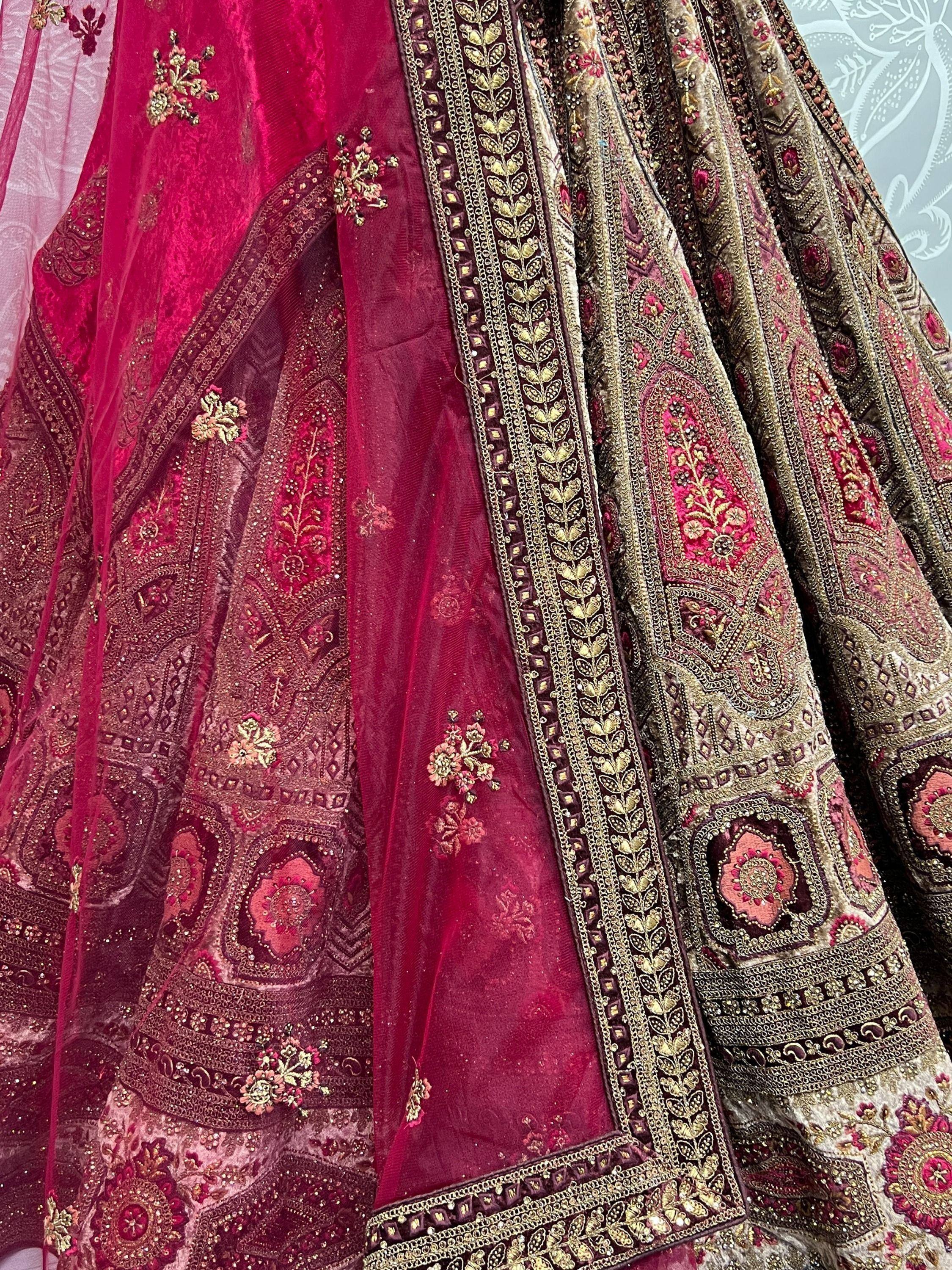 Luxury maroon velvet lehenga choli with heavy gold embroidery and floral motifs, perfect for Indian weddings.