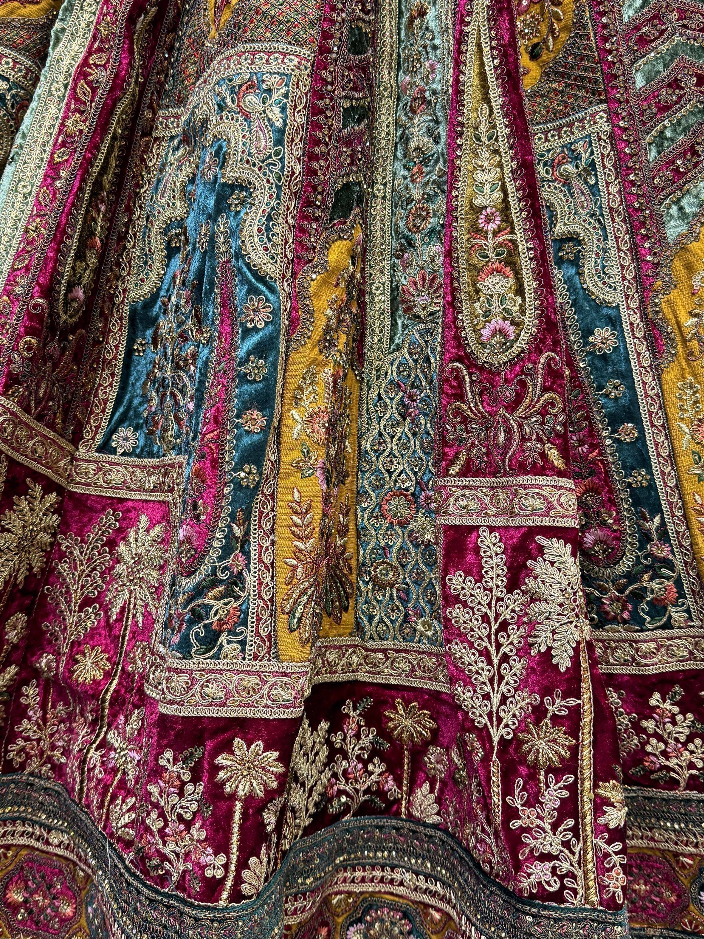 Luxury Indian ethnic lehenga with intricate gold embroidery, velvet fabric, and vibrant floral patterns in maroon, teal, and gold.