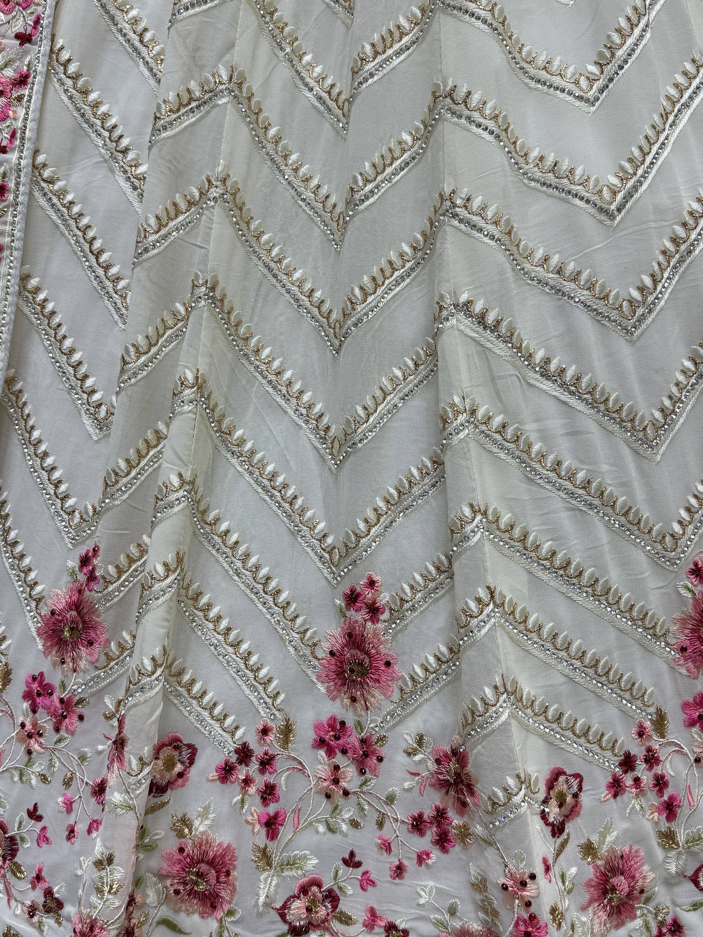 White ethnic gown with pink floral embroidery and gold chevron detailing, perfect for Indian occasions.