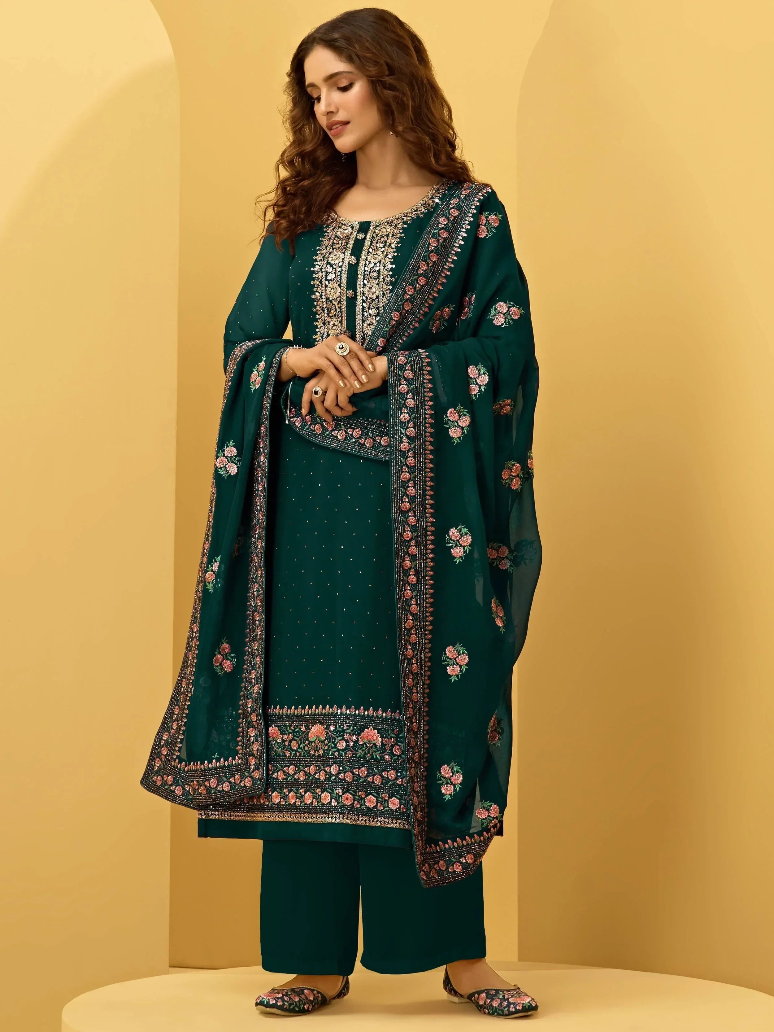 Woman wearing a dark green embroidered salwar kameez with floral dupatta and matching juttis