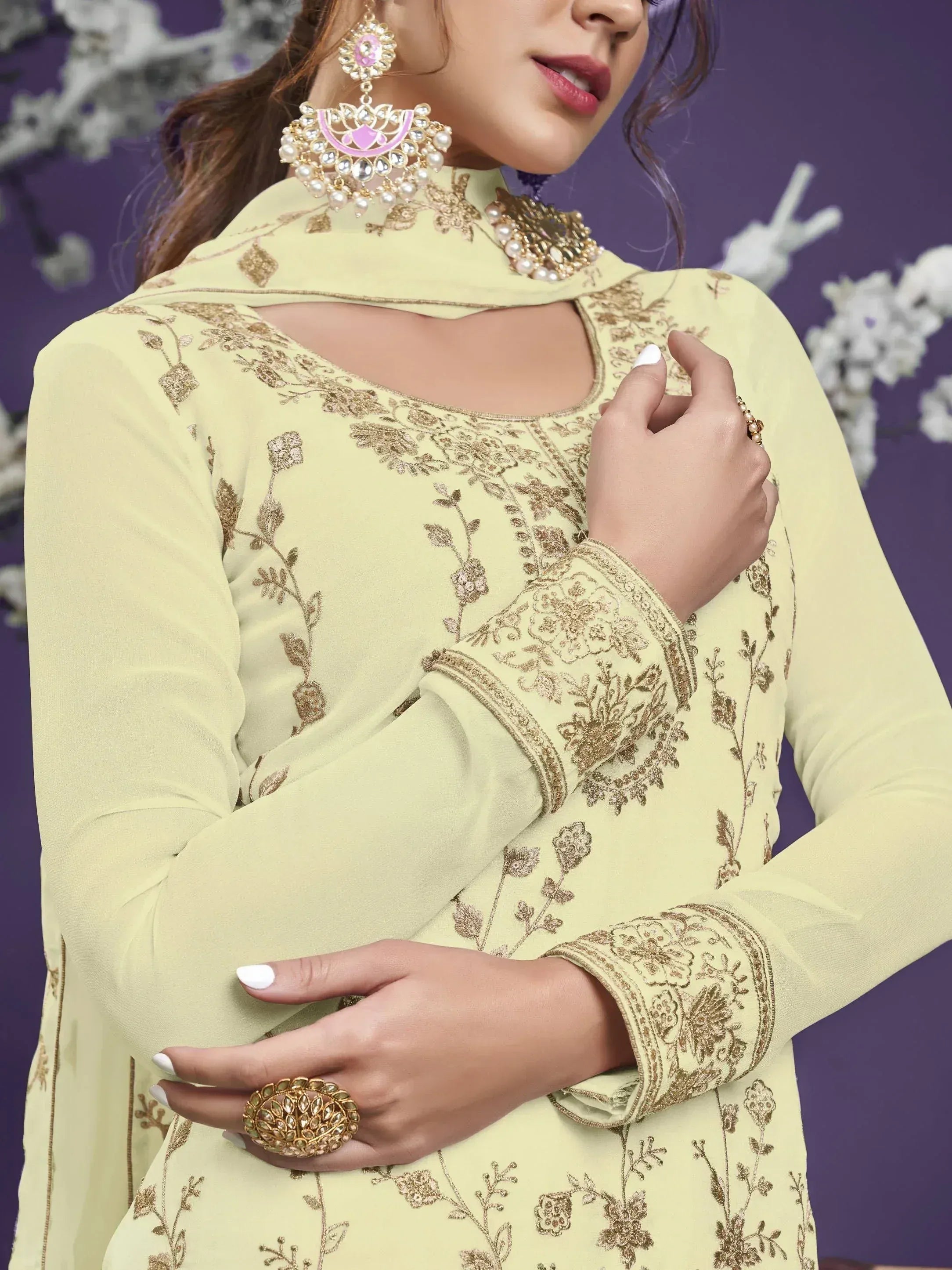 Woman in pastel yellow embroidered salwar kameez with gold jewelry and floral details