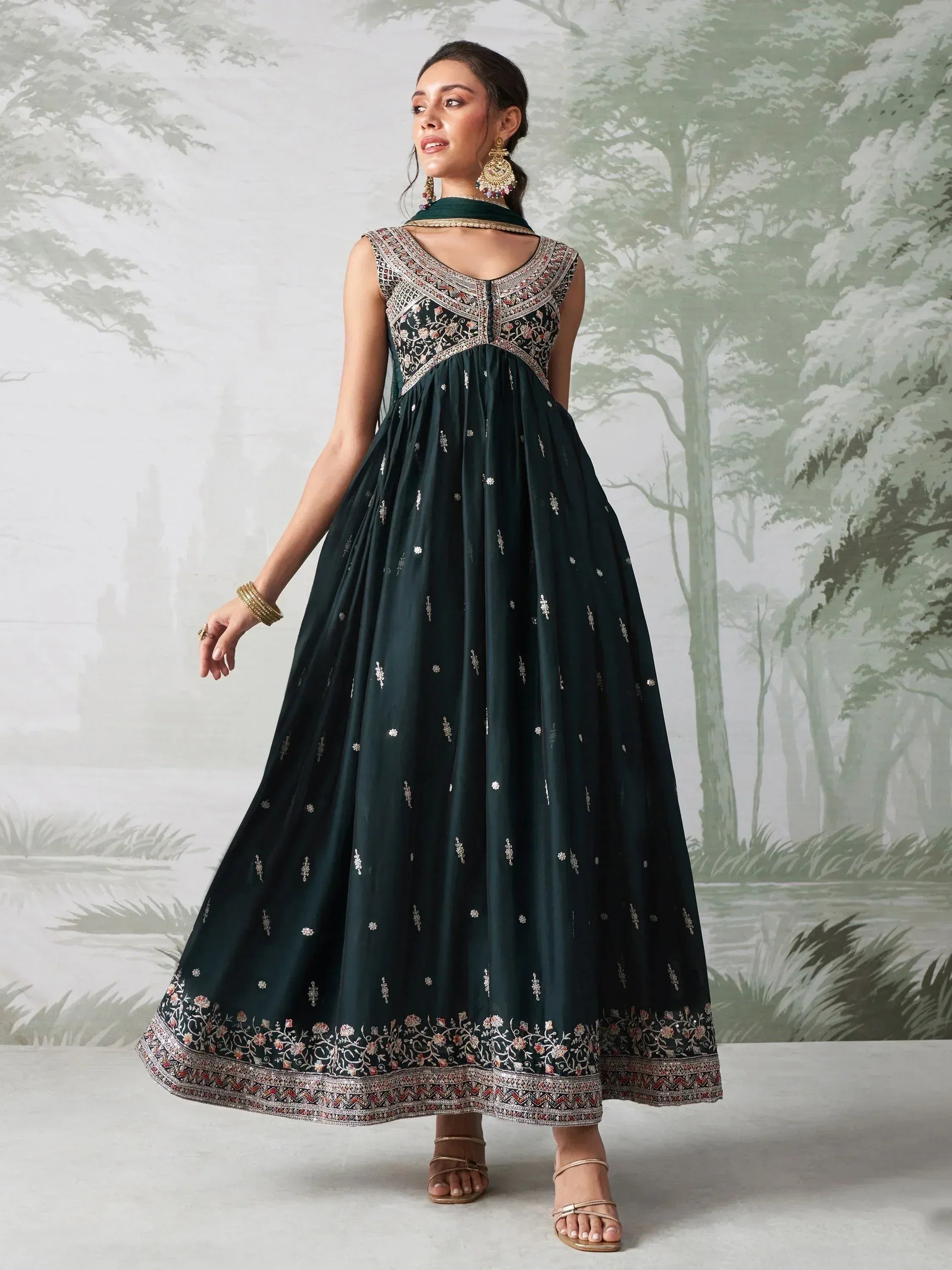 Woman wearing sleeveless dark green embroidered Indian ethnic gown, standing indoors