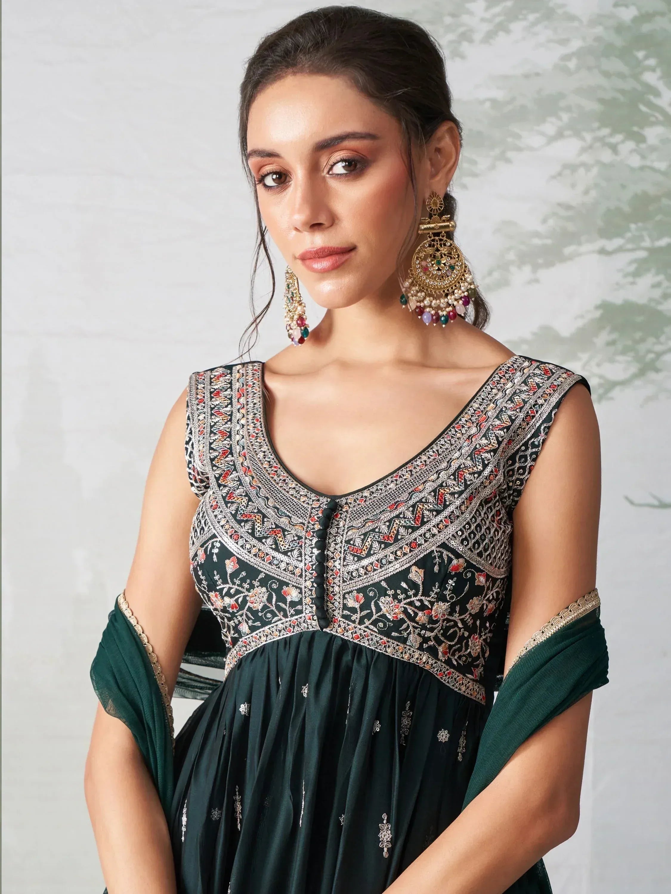 Woman wearing dark green embroidered ethnic gown with sleeveless design and statement earrings