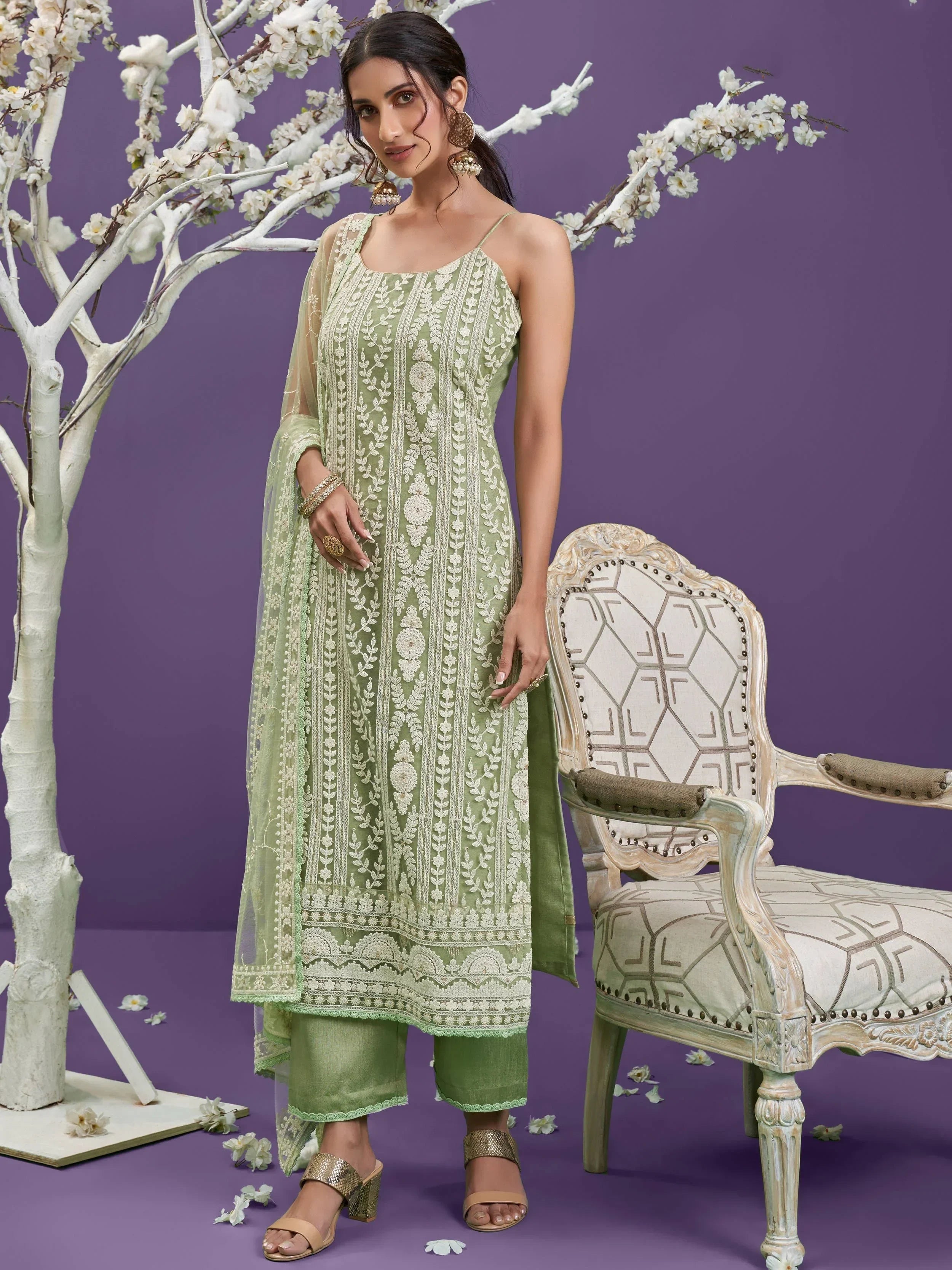 Woman in green embroidered Lucknowi salwar kameez with dupatta, standing by a chair