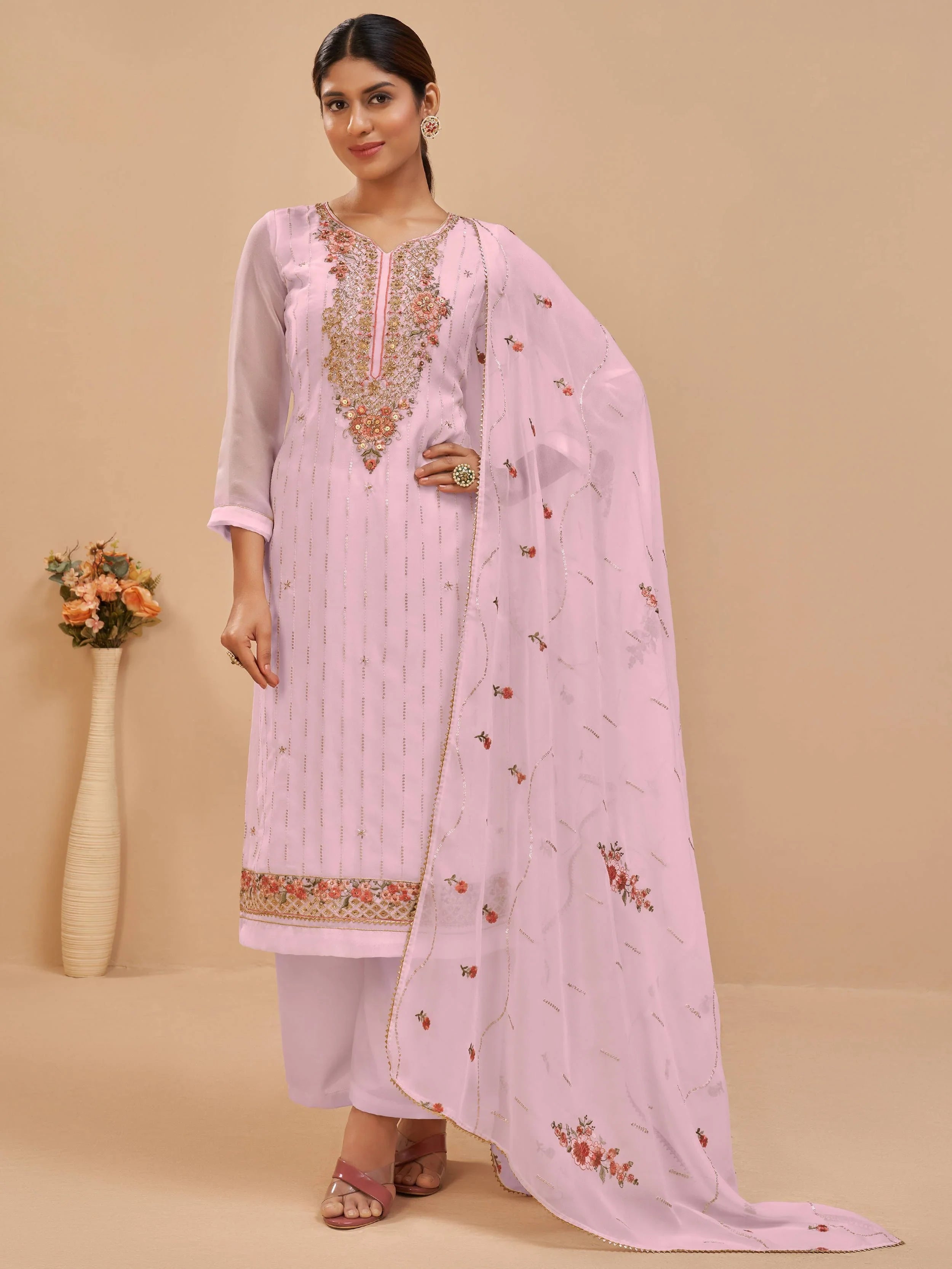 Woman in light pink embroidered salwar kameez with floral dupatta, standing indoors