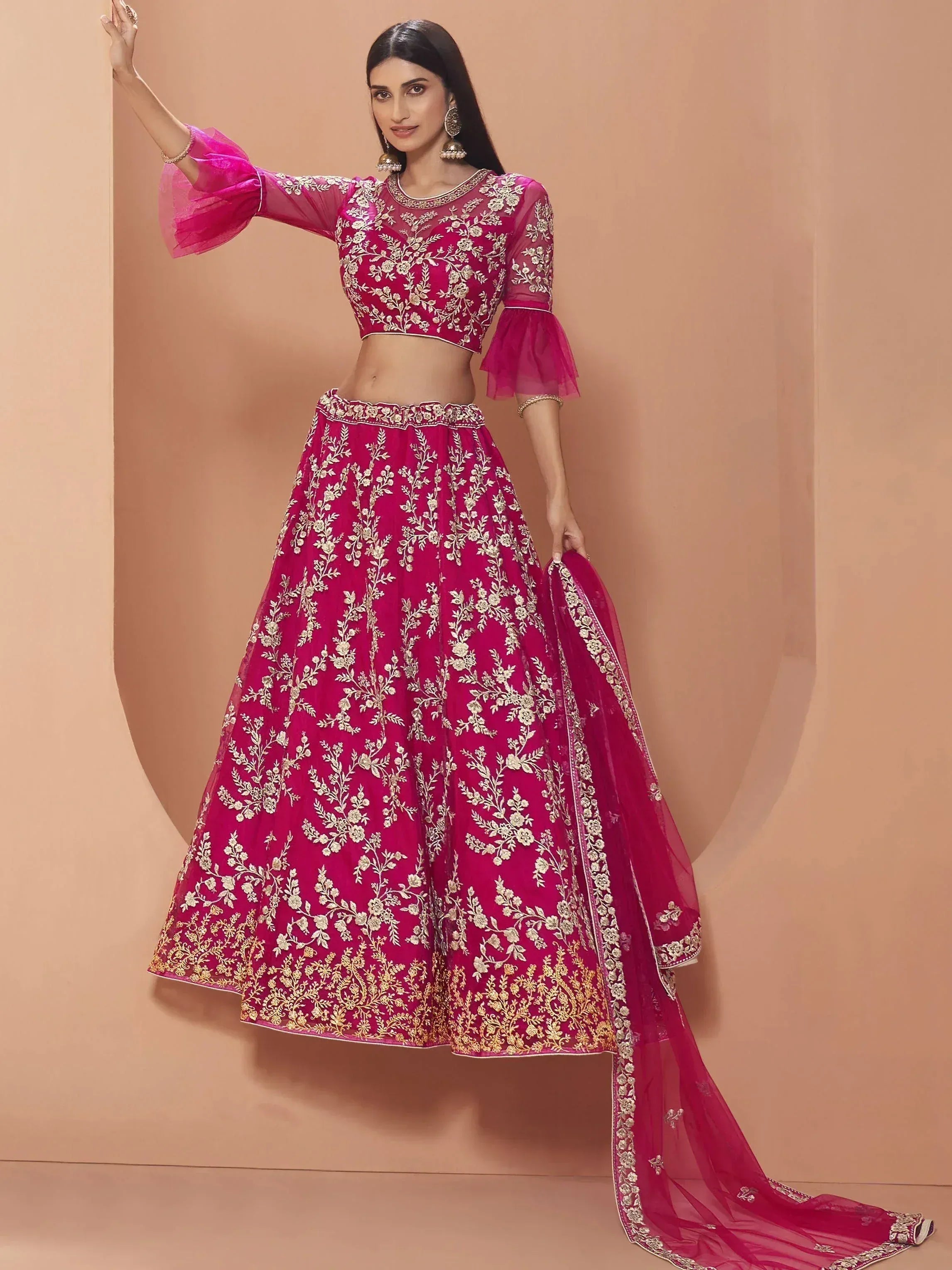 Fuchsia pink embroidered lehenga choli with gold floral work, sheer bell sleeves, and matching dupatta for Indian ethnic wear.