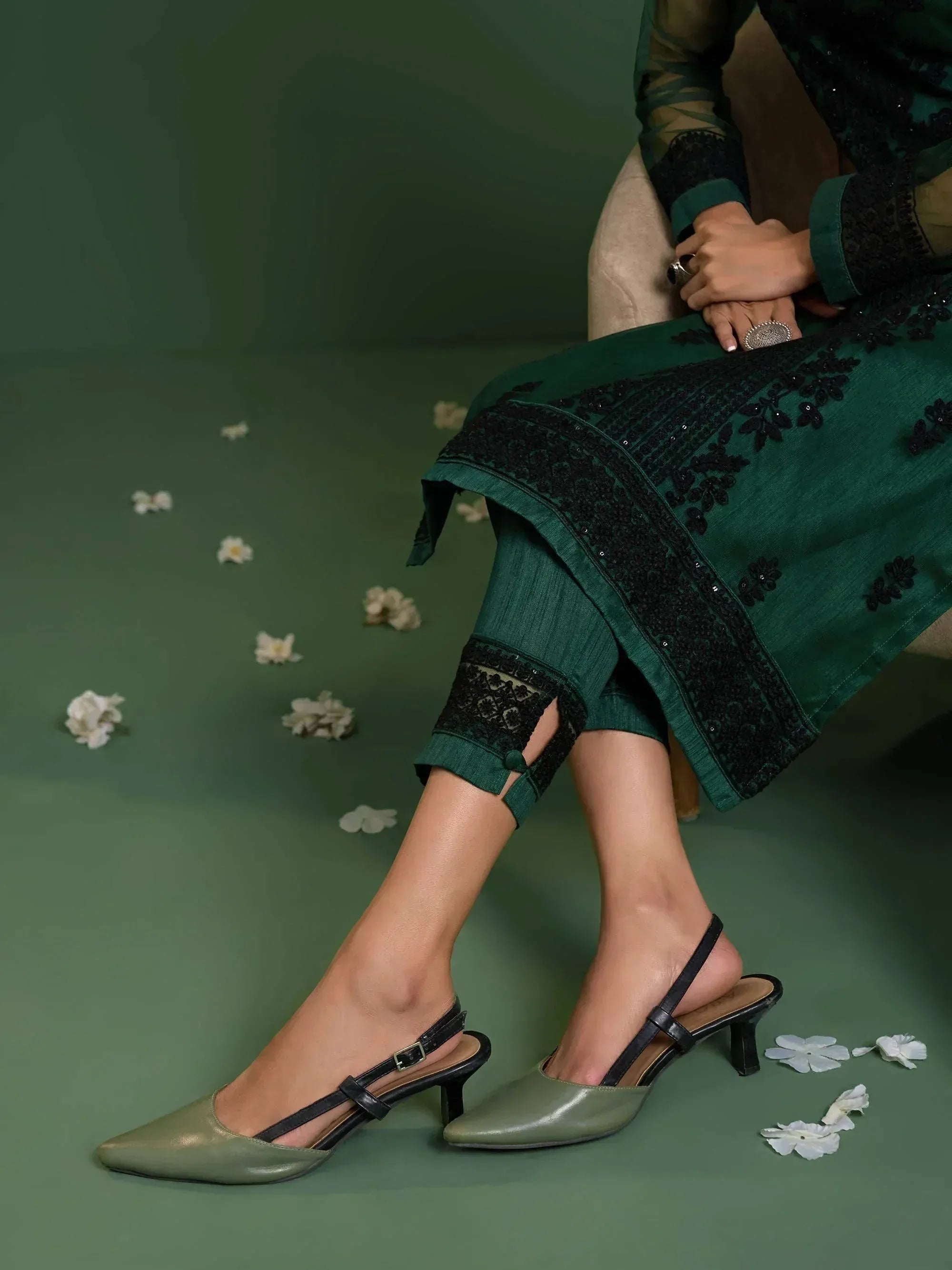 Emerald green ethnic salwar kameez with black lace, paired with olive heels and scattered white flowers.