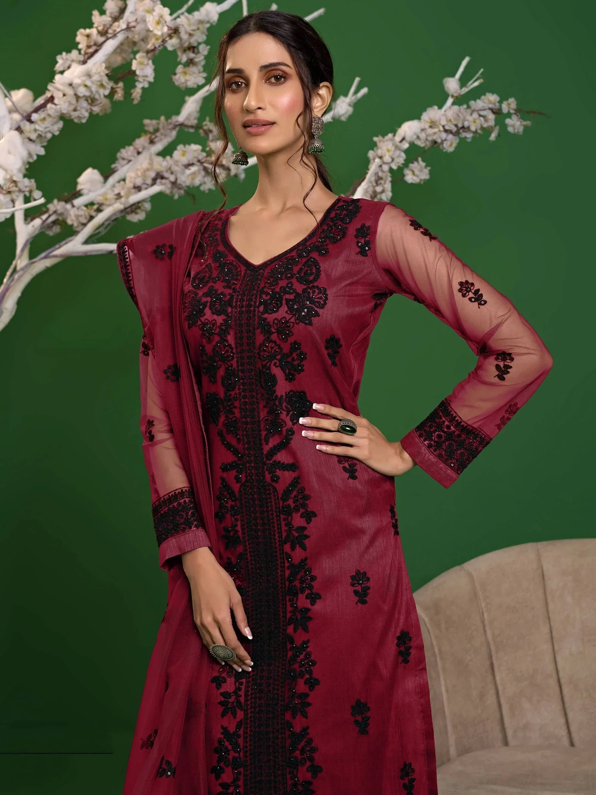 Woman wearing maroon embroidered designer salwar kameez with dupatta, floral background