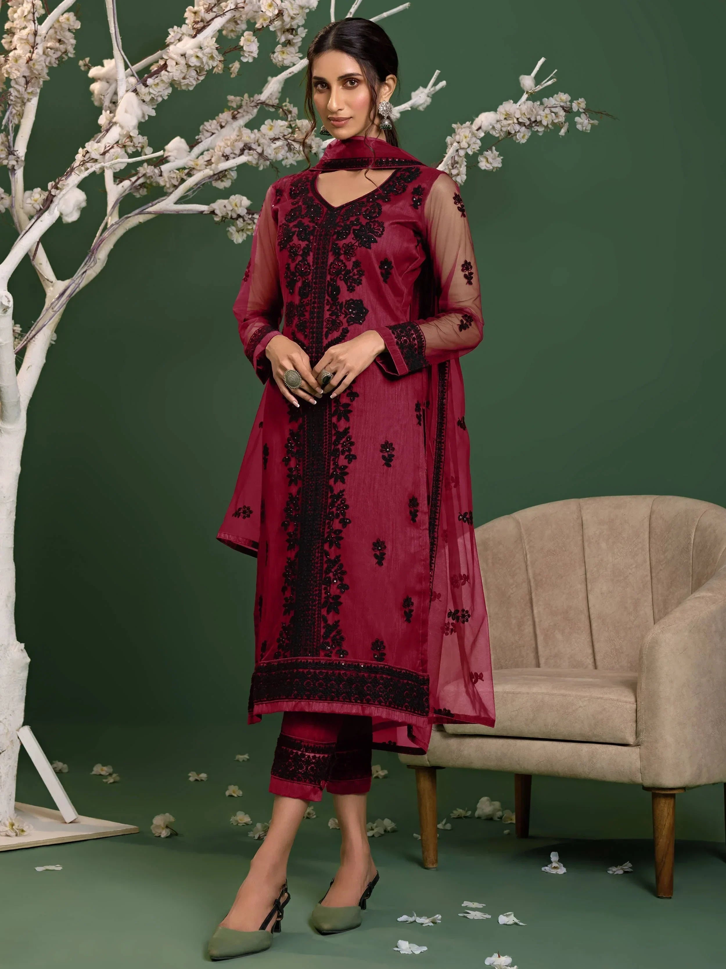 Woman in maroon embroidered salwar kameez with sheer sleeves, standing by floral decor