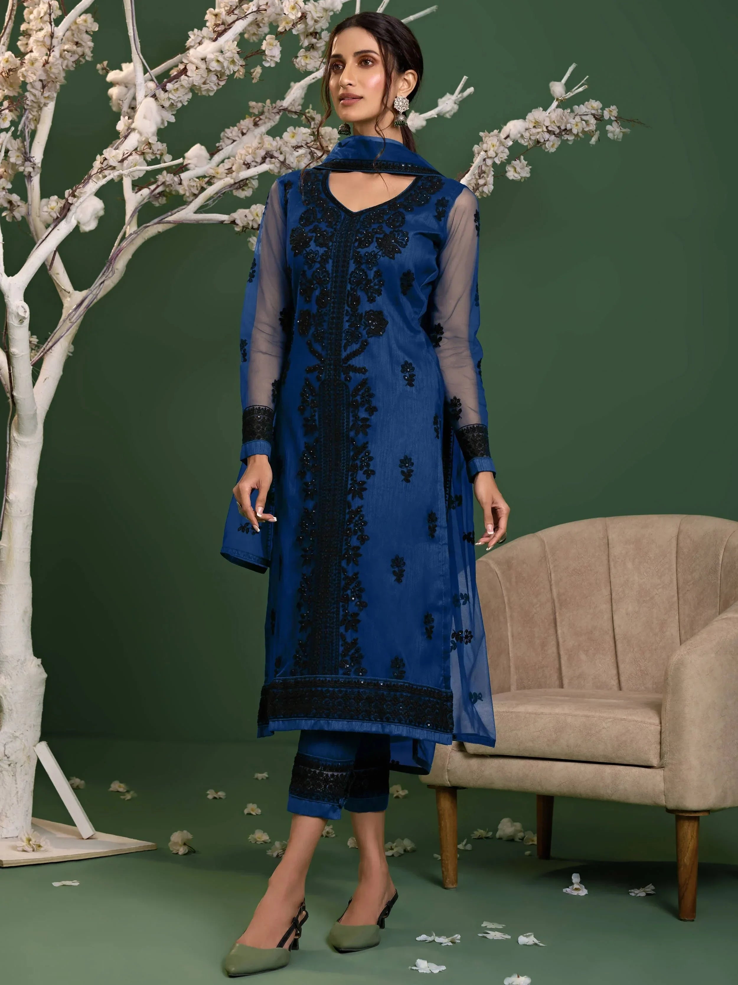 Woman wearing blue embroidered salwar kameez with sheer sleeves and churidar, standing indoors